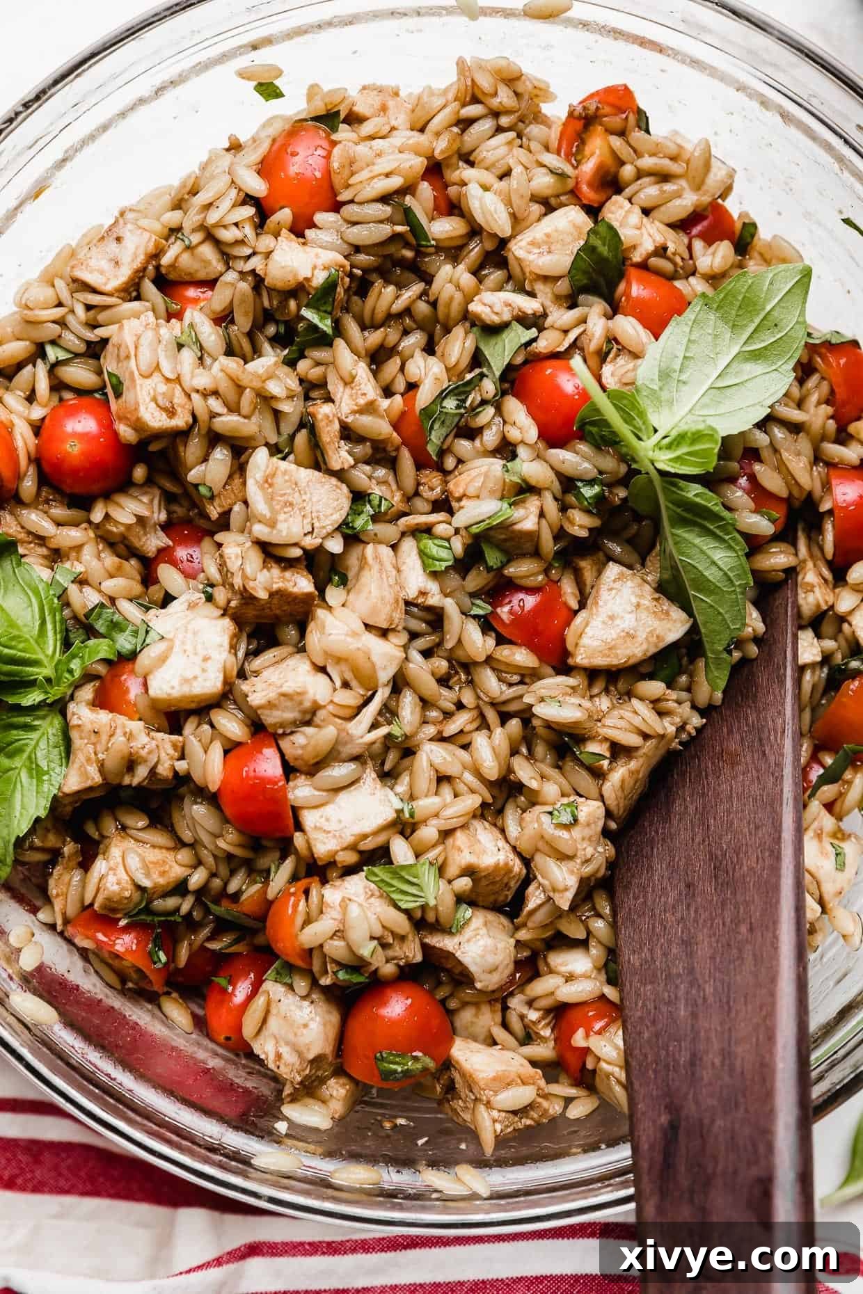 A vibrant and refreshing chicken orzo caprese salad presented in a clear glass bowl, artfully arranged on a clean white background.