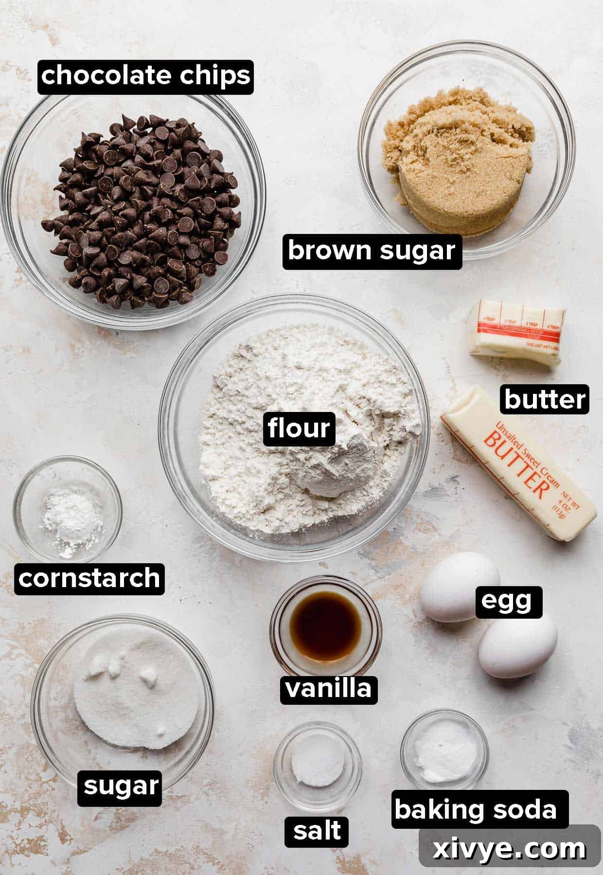 Ultimate Chocolate Chip Cookie Cake 3 Chocolate Chip Cookie Cake ingredients portioned into glass bowls on a white textured background.