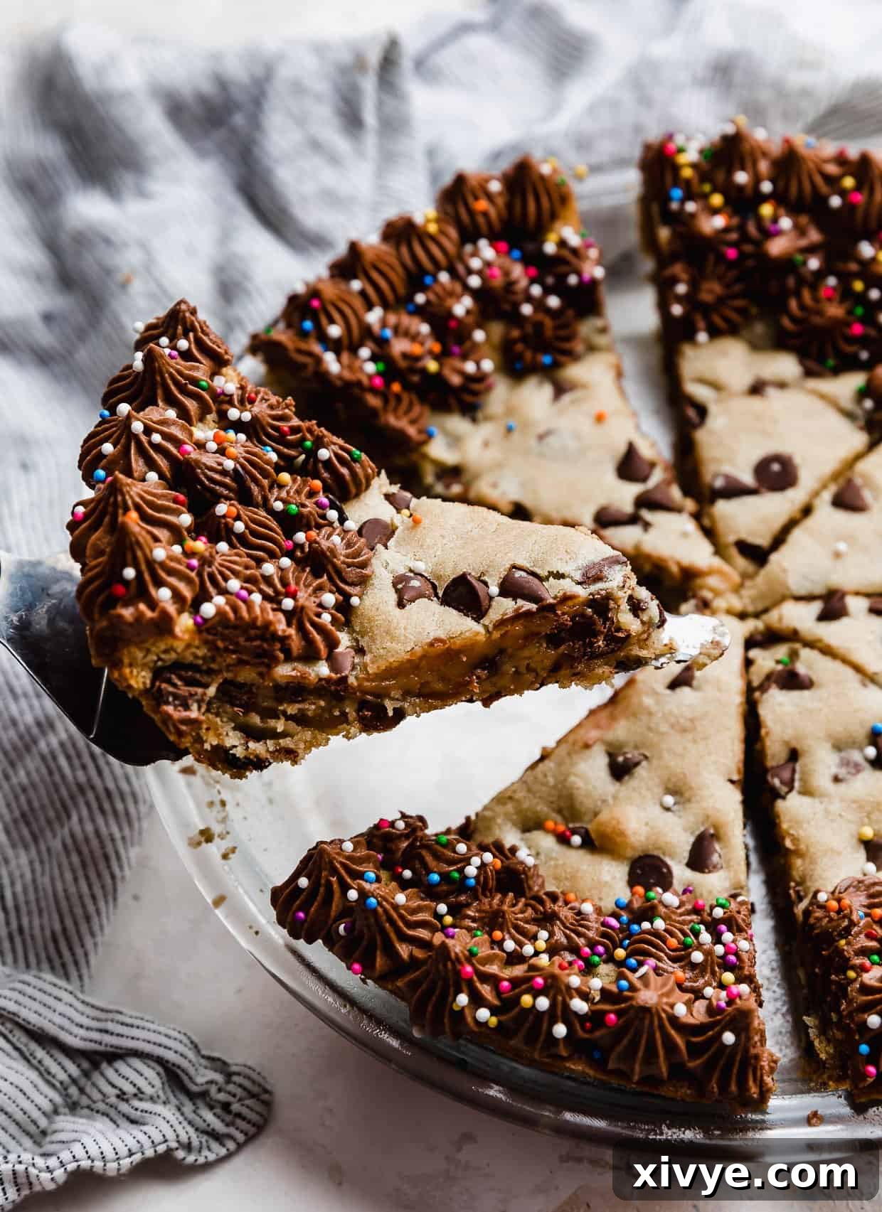 Ultimate Chocolate Chip Cookie Cake 10 A slice of cookie cake with chocolate frosting along the edges, on a serving spatula.
