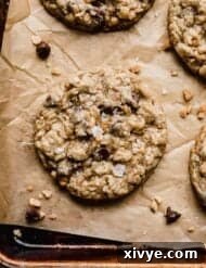 Crumbl mom's recipe cookie on a baking sheet with toffee bits and chocolate chips near the cookie.