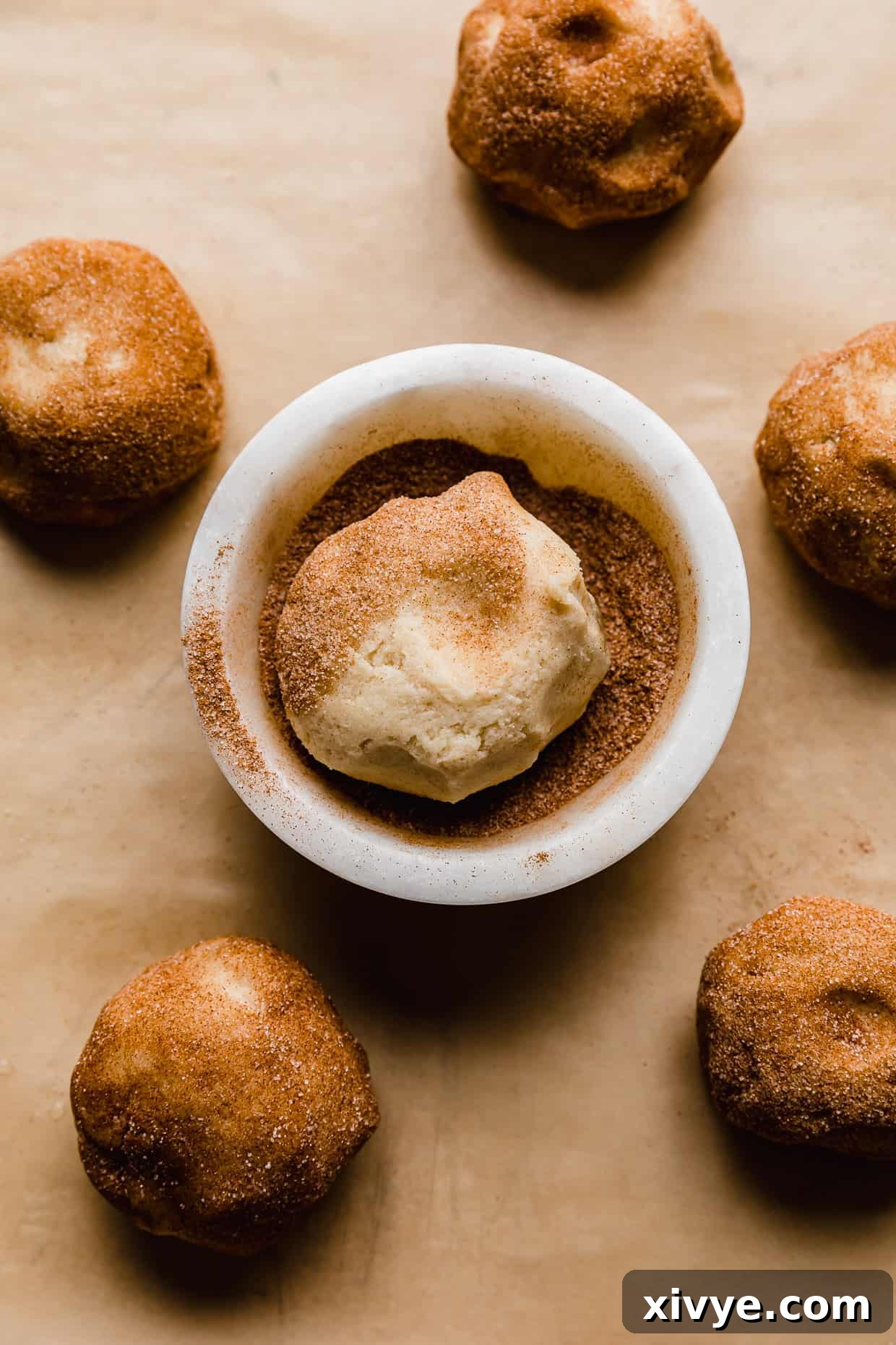 Your Ultimate Crumbl Snickerdoodle Copycat Recipe 5 A cookie dough ball in a bowl filled with cinnamon sugar.