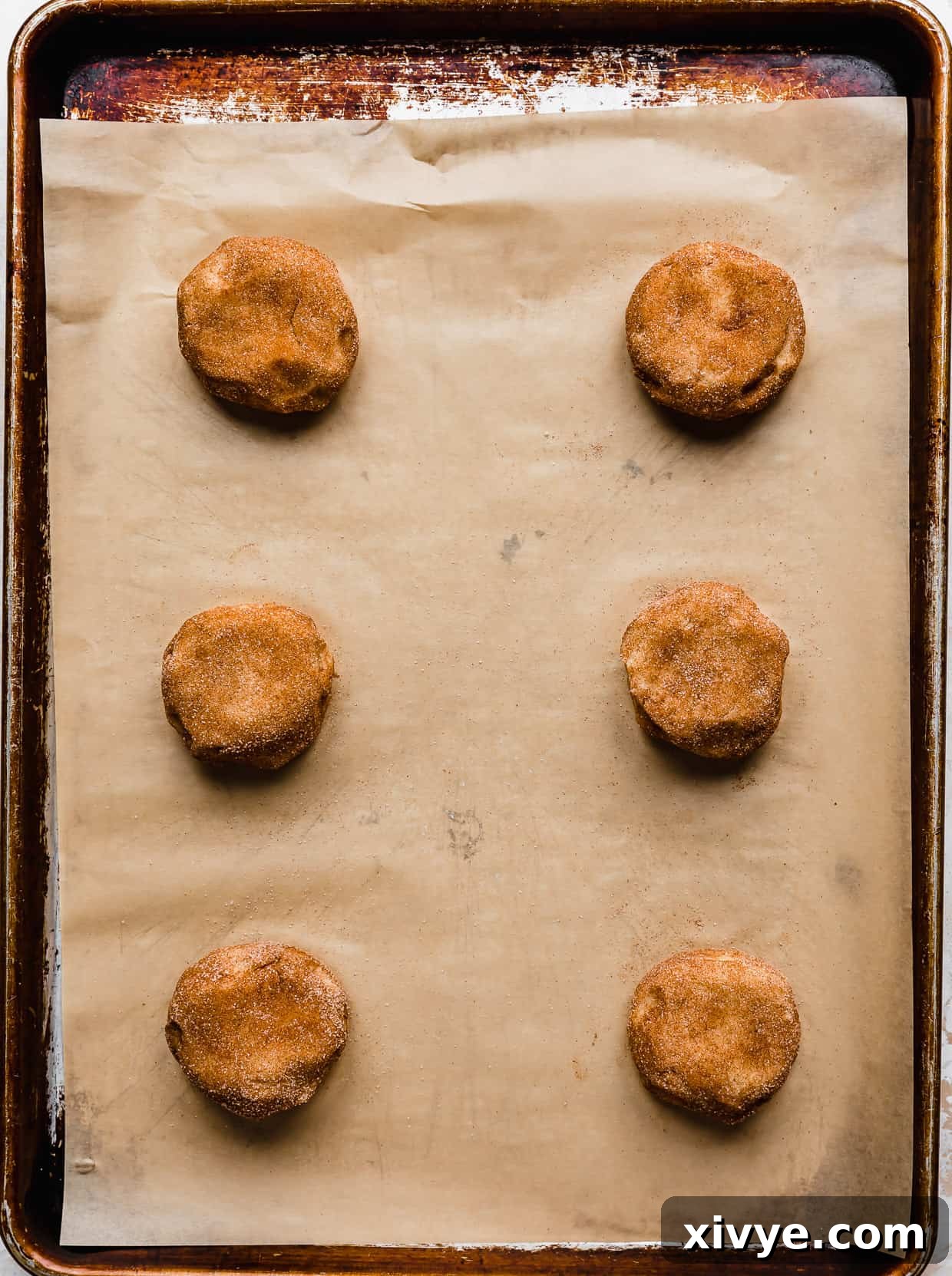 Your Ultimate Crumbl Snickerdoodle Copycat Recipe 6 Six Crumbl Snickerdoodle cookie dough balls on a tan parchment paper.