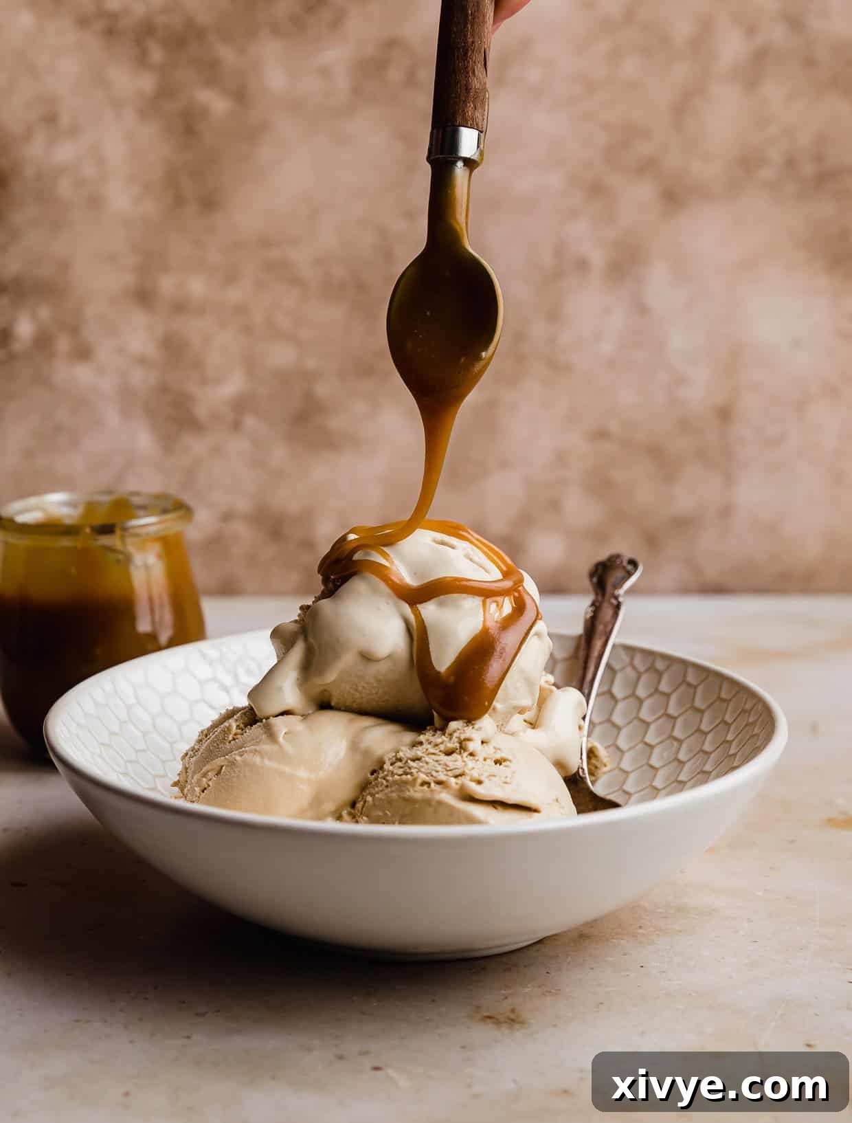 Velvet Butterscotch Indulgence 8 Butterscotch Ice Cream in a white bowl with a spoon drizzling homemade Butterscotch sauce overtop.