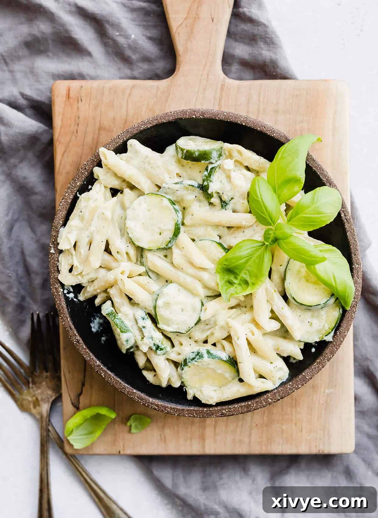 A black bowl with Summer Zucchini pasta with ricotta and basil, garnished with fresh basil leaves and parmesan cheese.