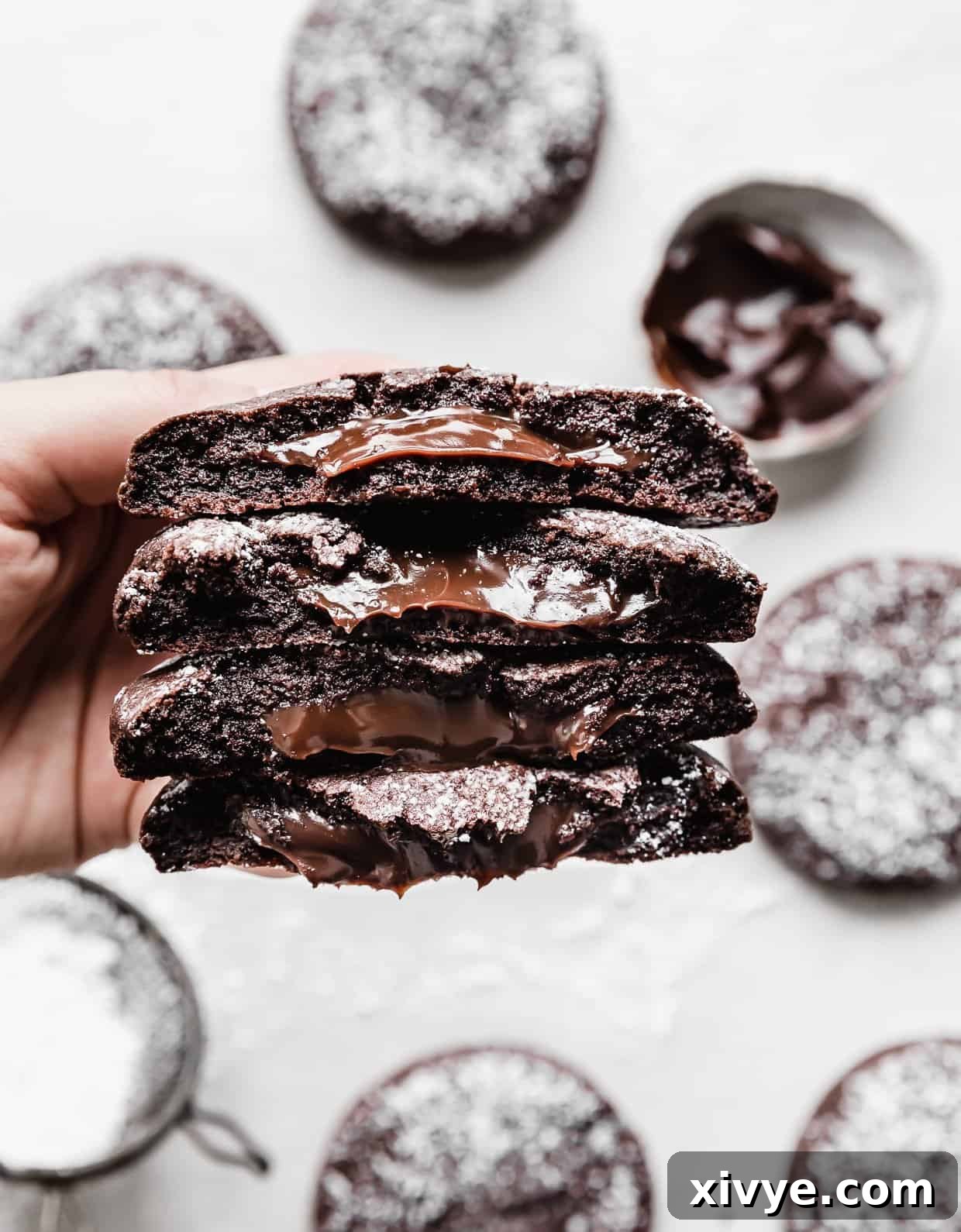 A hand holding four chocolate molten lava cookie halves, with rich, dark hot fudge oozing from the centers of each half, highlighting the perfect molten texture.