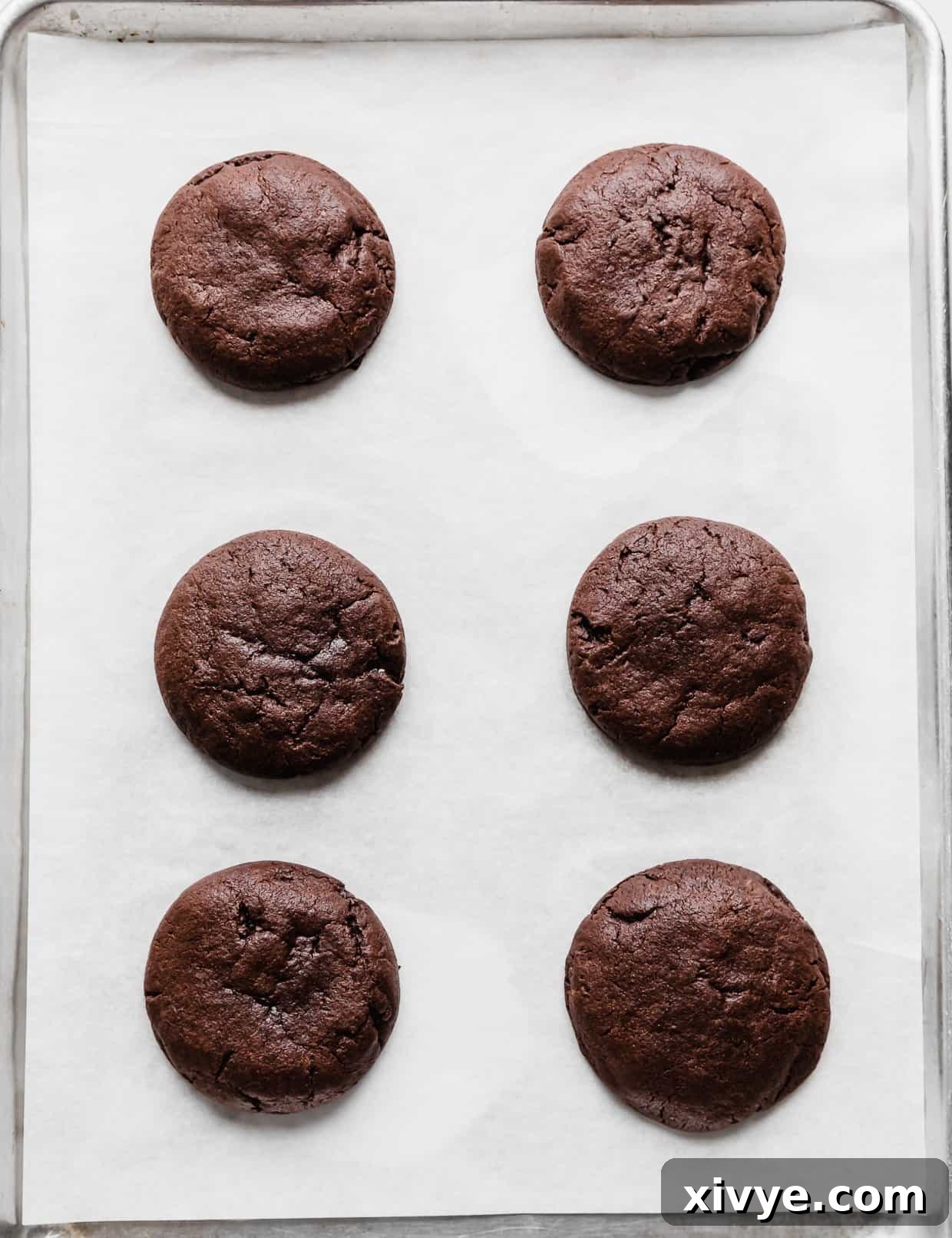 Six freshly baked chocolate molten lava cookies, with slightly soft centers, resting on white parchment paper.