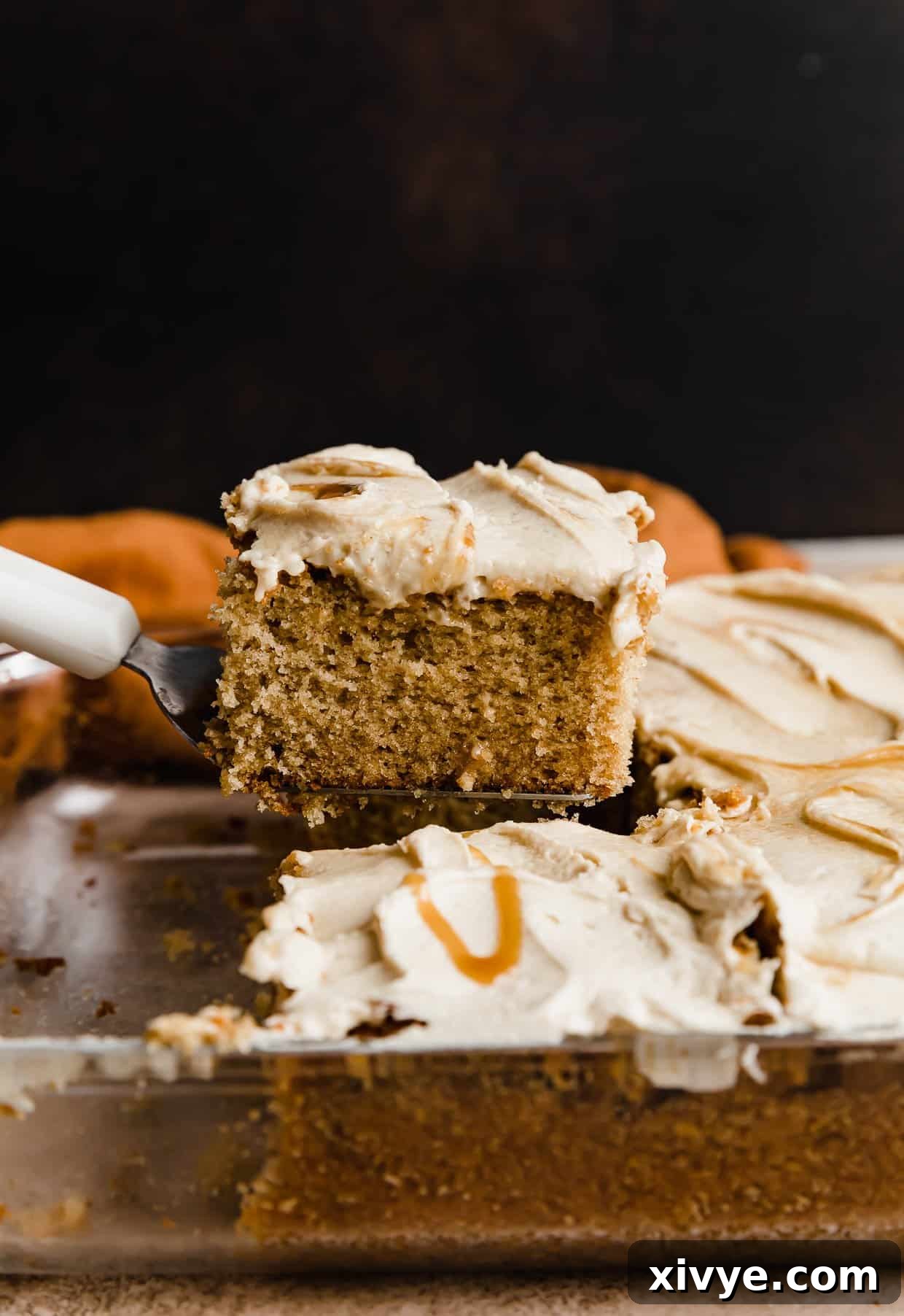 A spatula holding up a slice of square Butterscotch Cake against a brown background.