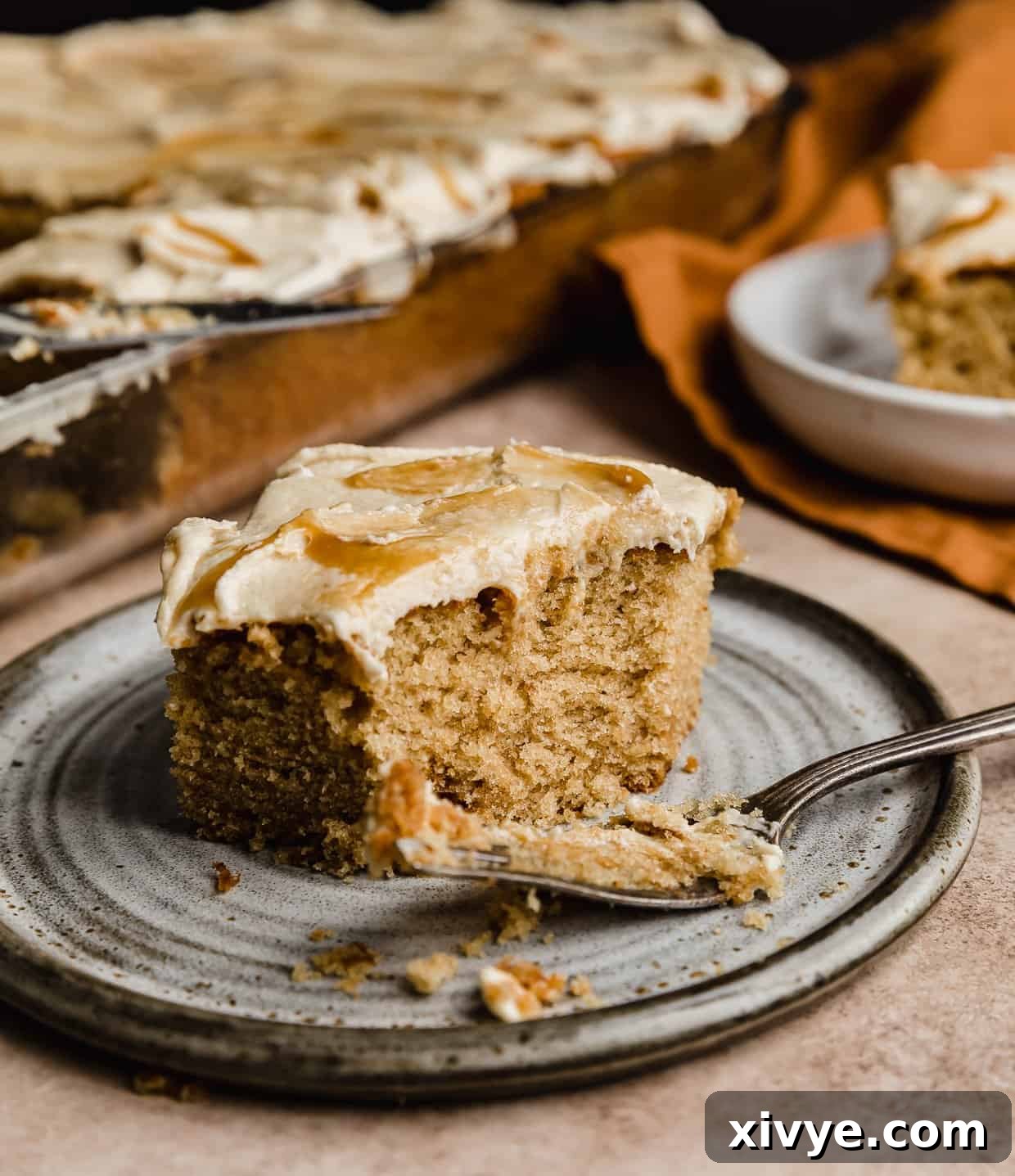 A square slice of Butterscotch Cake on a gray plate with a fork near the cake.