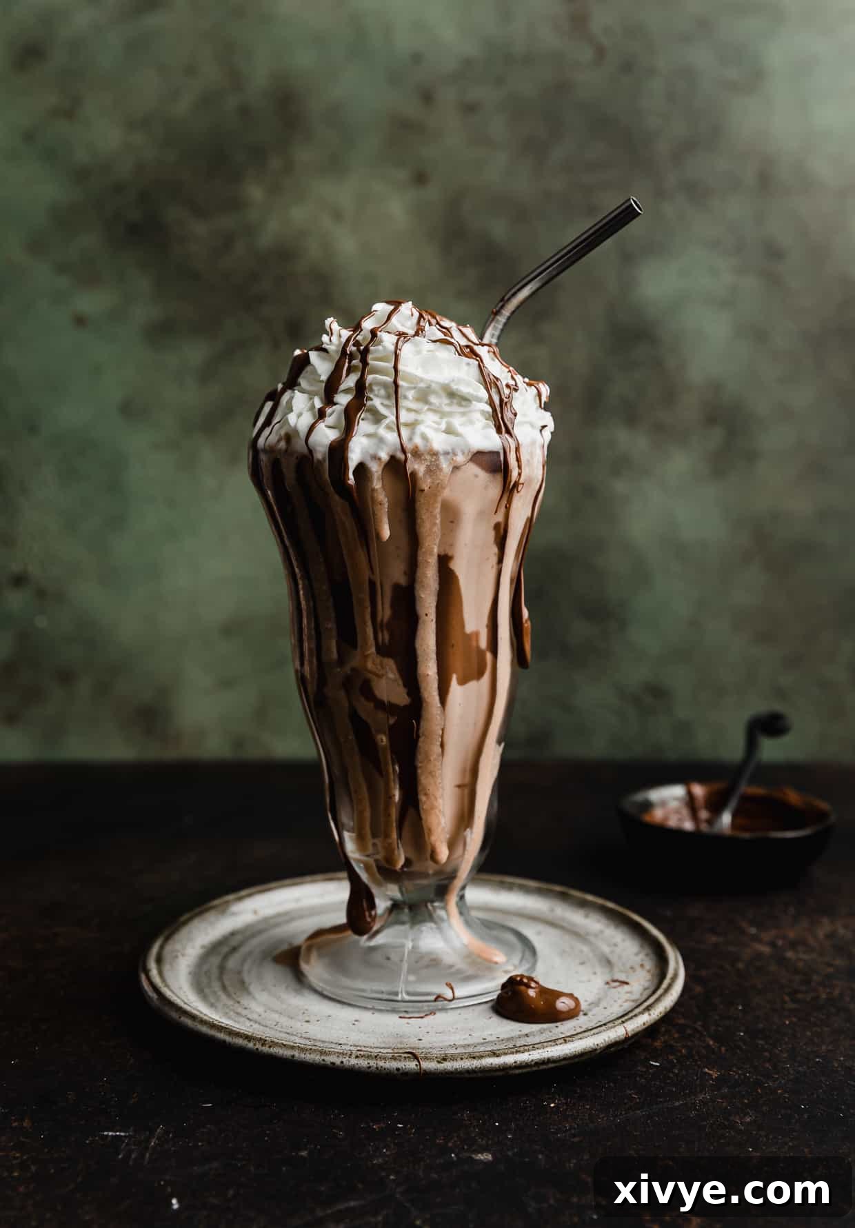 A beautifully presented Nutella Milkshake in a clear glass cup, showcasing its rich, creamy texture, set against a dark green textured background.
