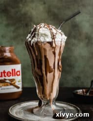 A perfectly blended Nutella Milkshake, served in a glass and garnished, against a dark green background.