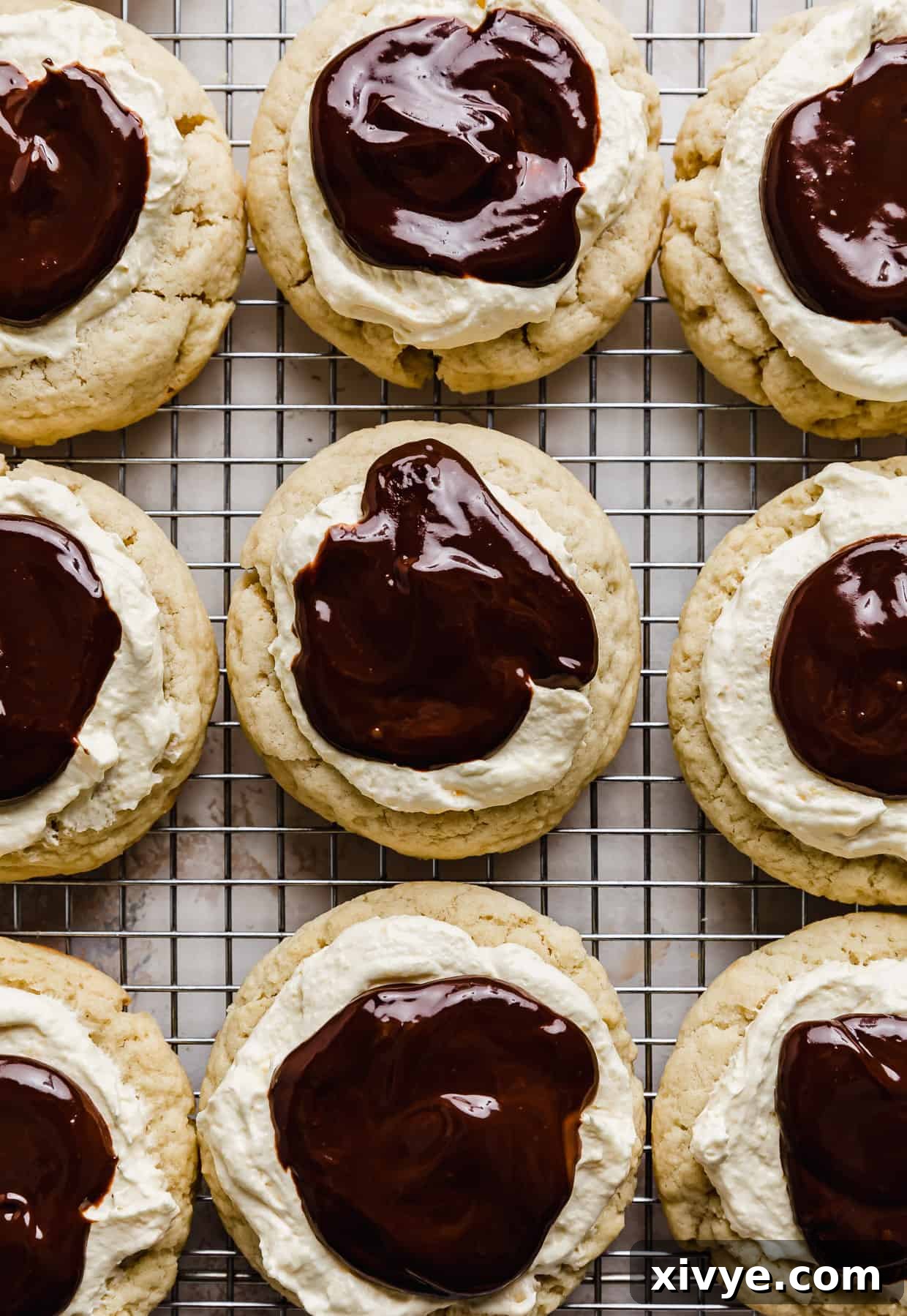 Chocolate ganache covered pastry cream topped cookies cooling on a wire rack.
