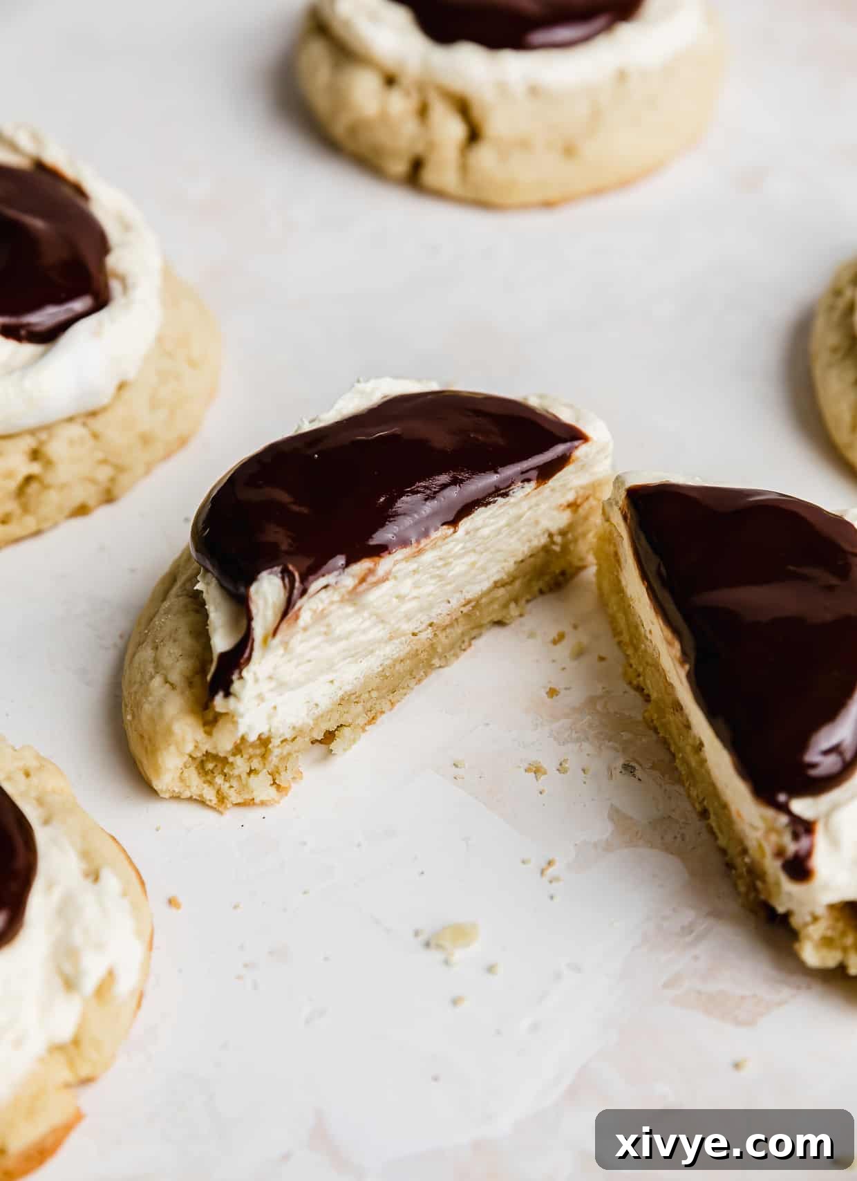 A Boston Cream Pie Cookie cut in half, showcasing the vanilla cookie, cream filling, and chocolate ganache.
