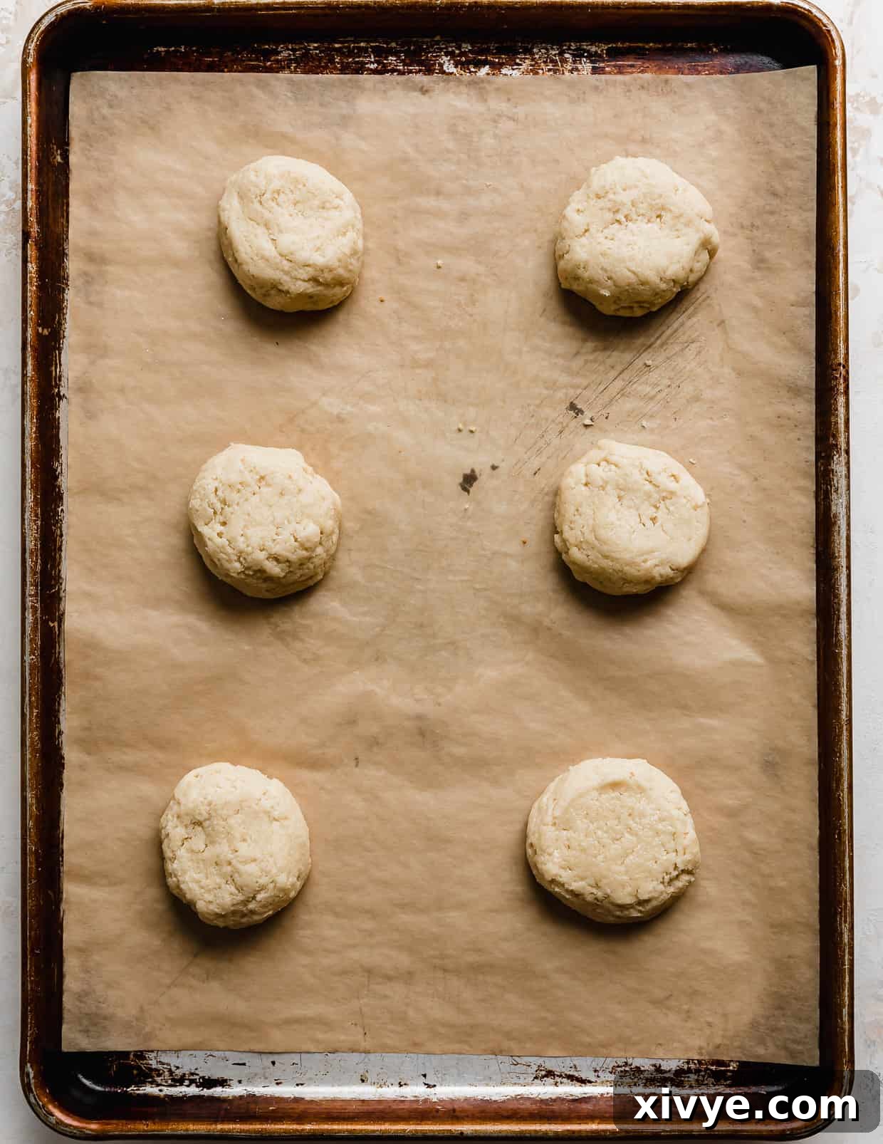 Six unbaked white cake sugar cookies on a parchment-lined baking sheet.