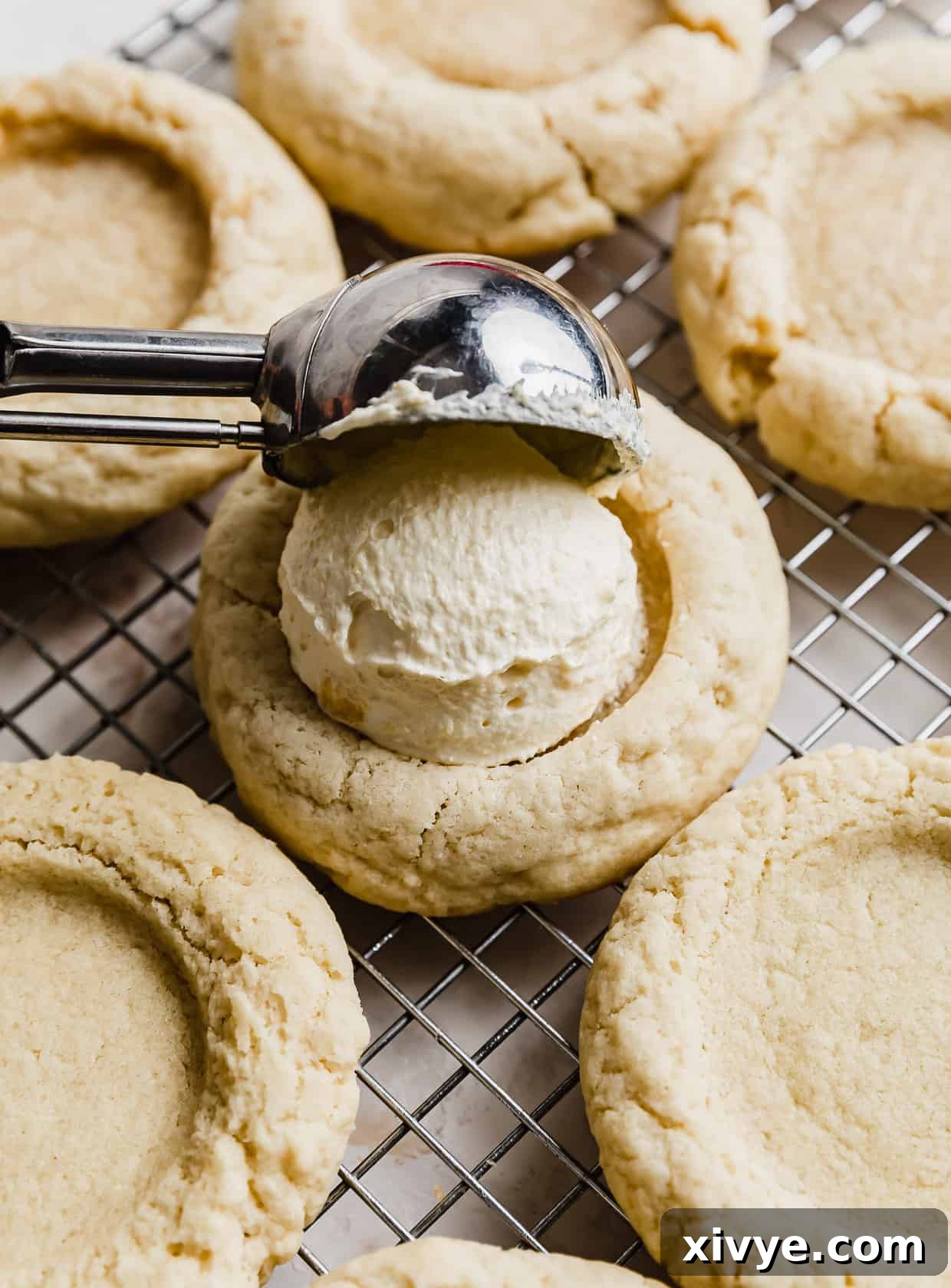 A cookie scoop portioning light yellow vanilla cream onto a cookie.