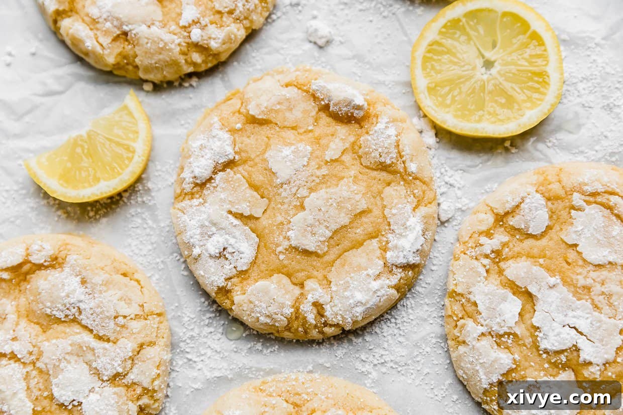 Zesty Lemon Crinkles 3 Freshly baked Lemon Crinkle Cookies on white parchment paper, garnished with vibrant lemon slices.
