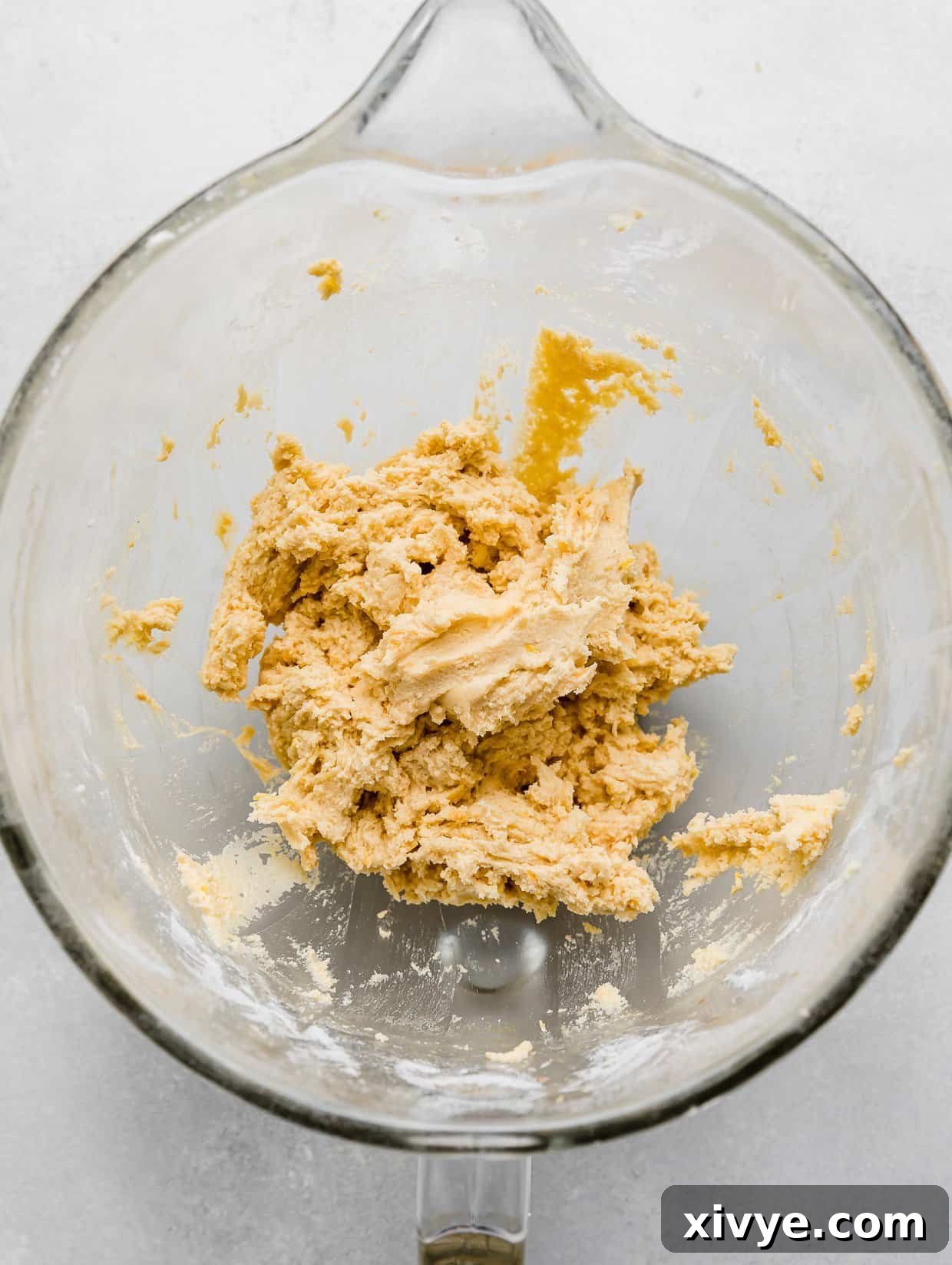Zesty Lemon Crinkles 5 Large Lemon Crinkle Cookie batter in a glass bowl on a light gray background, showing the uniform texture of the dough.