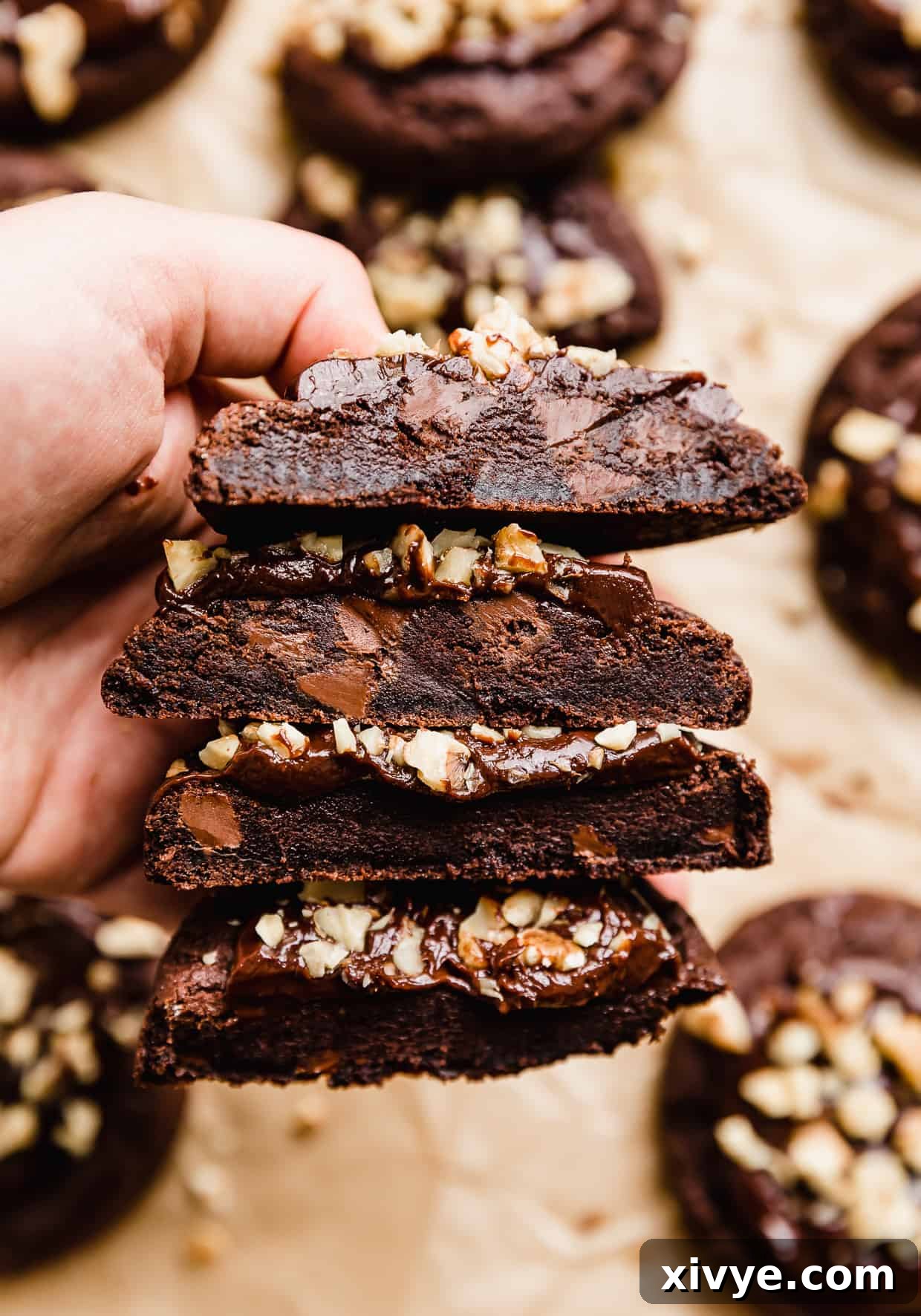 A hand holding 4 halves of Crumbl Walnut Fudge Brownie Cookies.