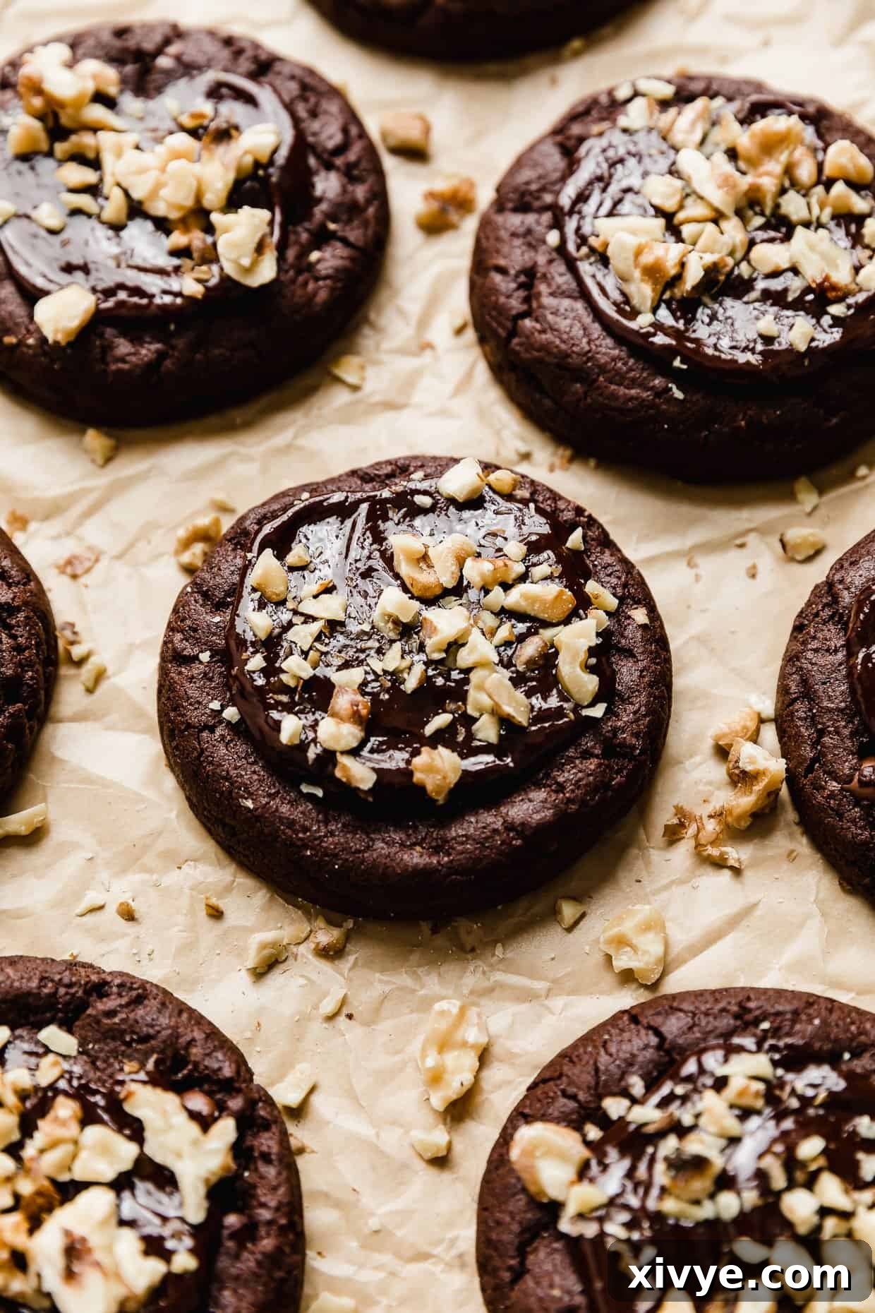 Crumbl Walnut Fudge Brownie Cookies topped with chopped walnuts on a tan parchment paper.