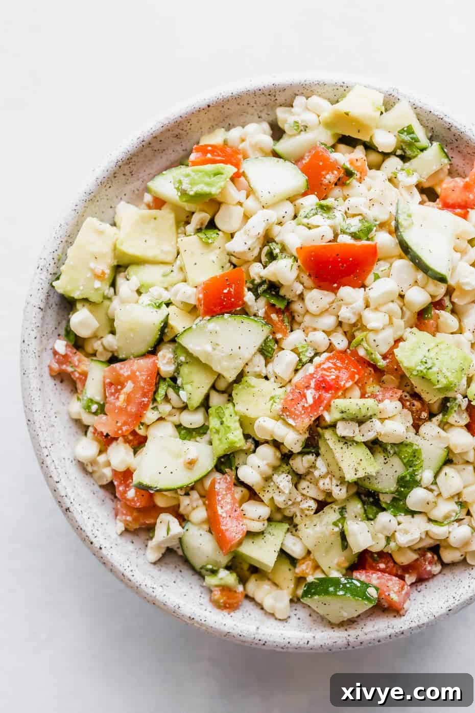 Close up image of a feta corn salad with chopped tomatoes, cucumber, corn, mint, and avocado.