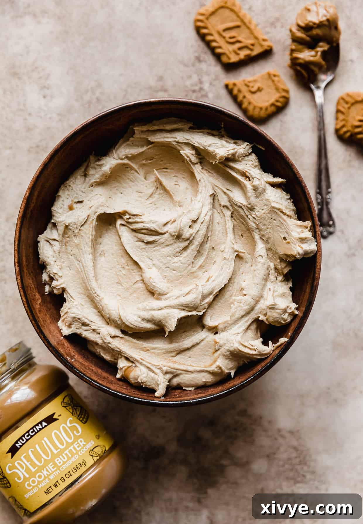 Cookie Butter Buttercream frosting made with Speculoos or Biscoff, in a brown bowl with Biscoff cookies crushed next to the bowl.