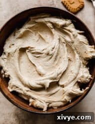 A brown bowl filled with a Biscoff Frosting on a textured tan and brown background.