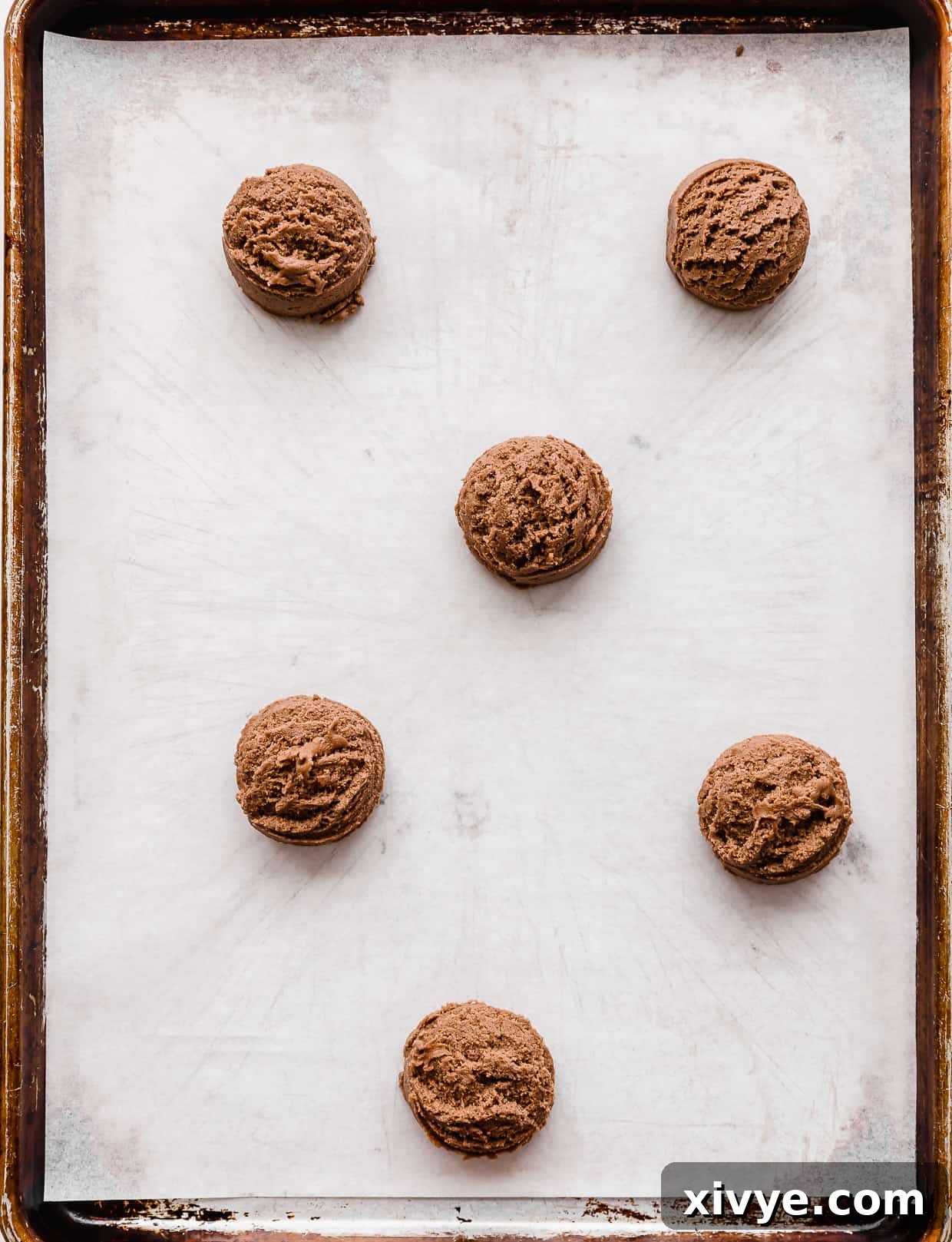 Six Nutella cookie dough balls perfectly arranged on a white parchment lined baking sheet, spaced for optimal baking.