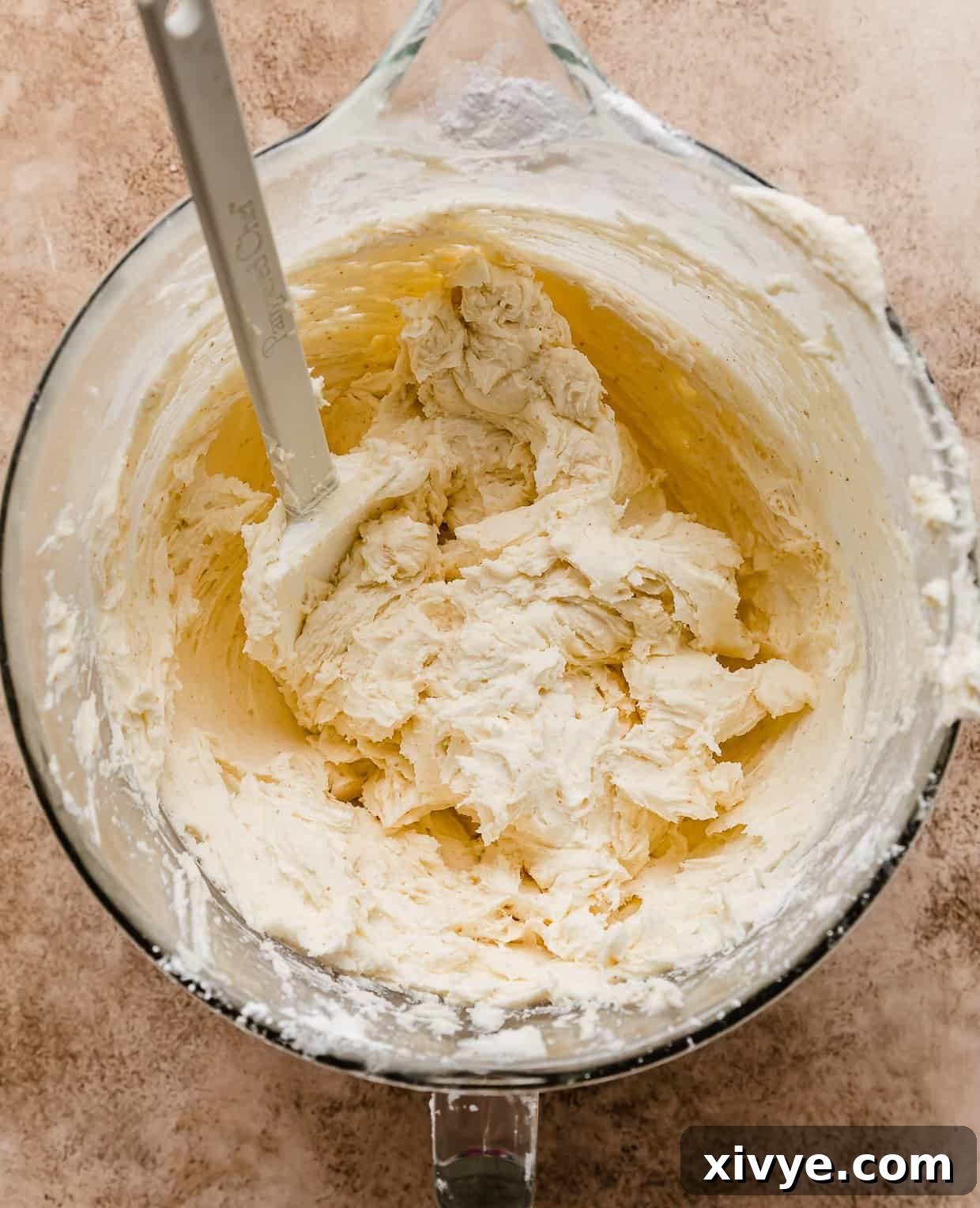Brown butter frosting in a glass bowl with a white spatula in the bowl.