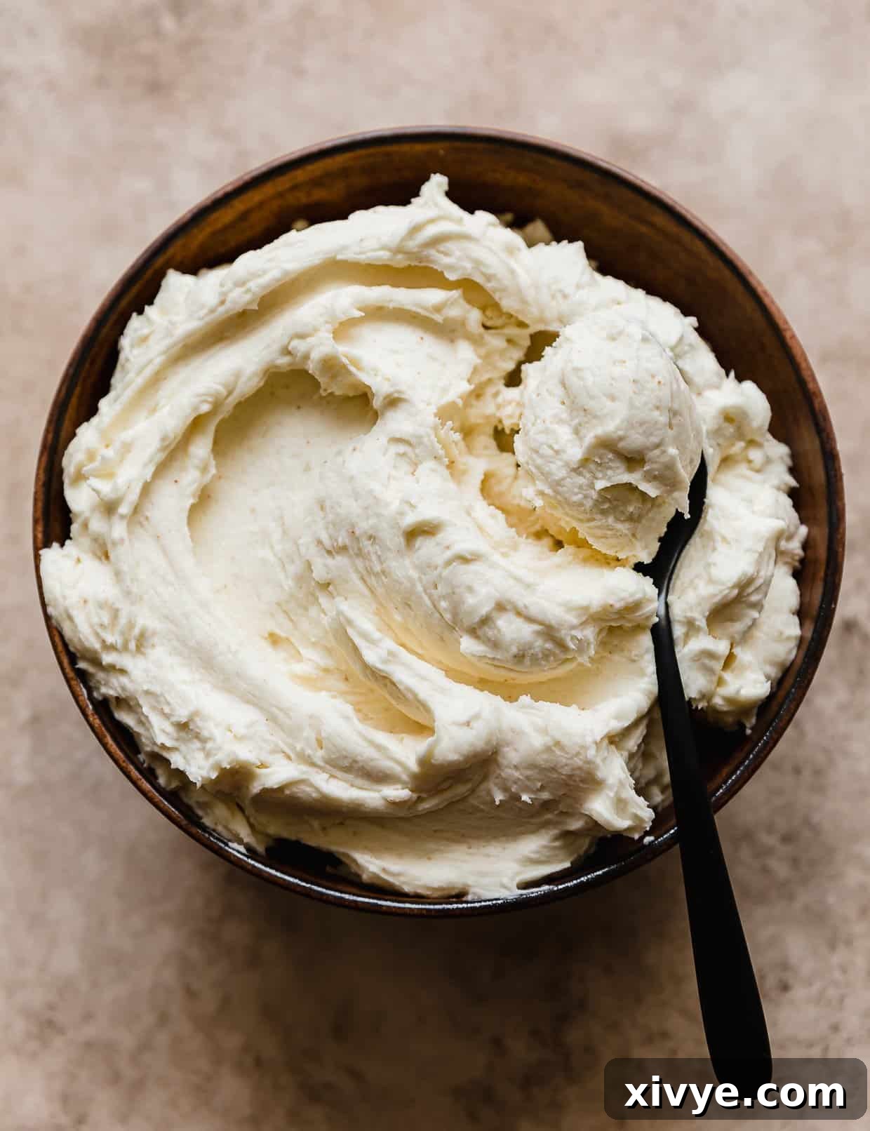 A black spoon in a bowl of brown butter frosting.