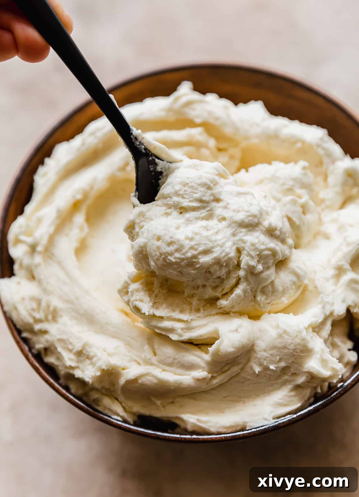 A spoon scooping brown butter frosting from a bowl filled with buttercream.