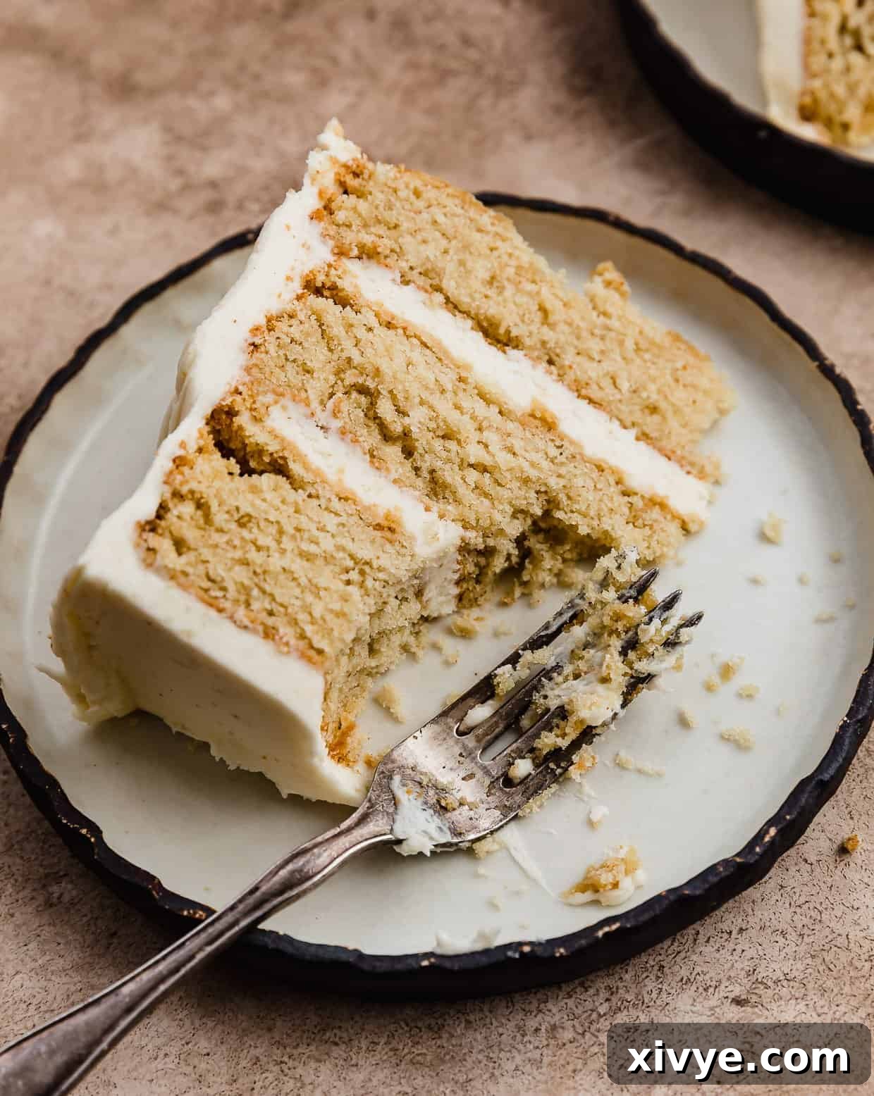 Toasted Butter Dream Cake 10 A fork next to a slice of Brown Butter Cake on a black rimmed white plate.