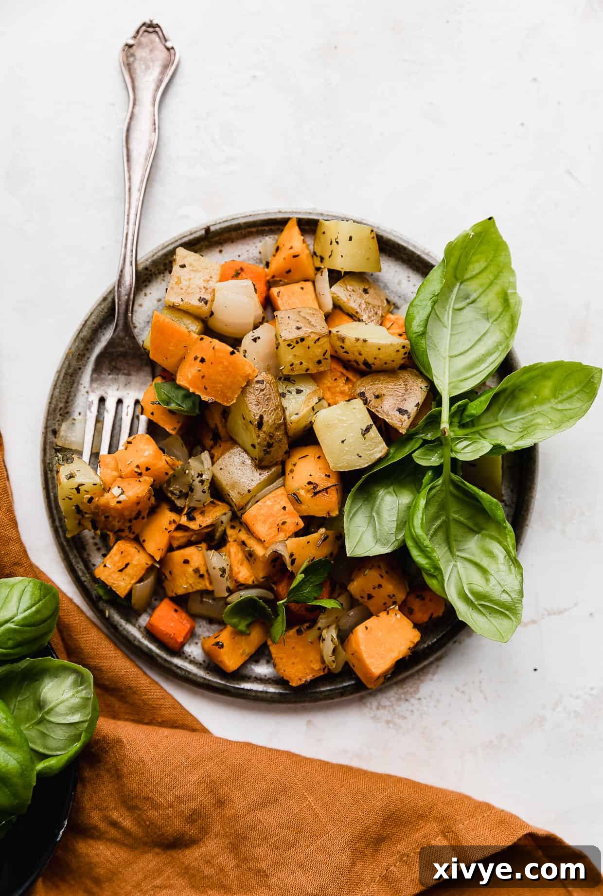 A gray plate on a white background with Sheet Pan Roasted Root Vegetables topped with fresh herbs on the plate, ready to be served.