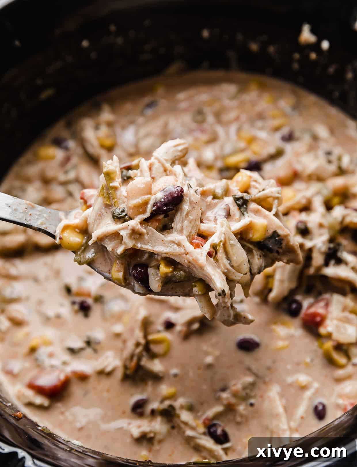A metal spoon with cream cheese chicken chili with black beans and corn on the spoon, ready to be eaten.