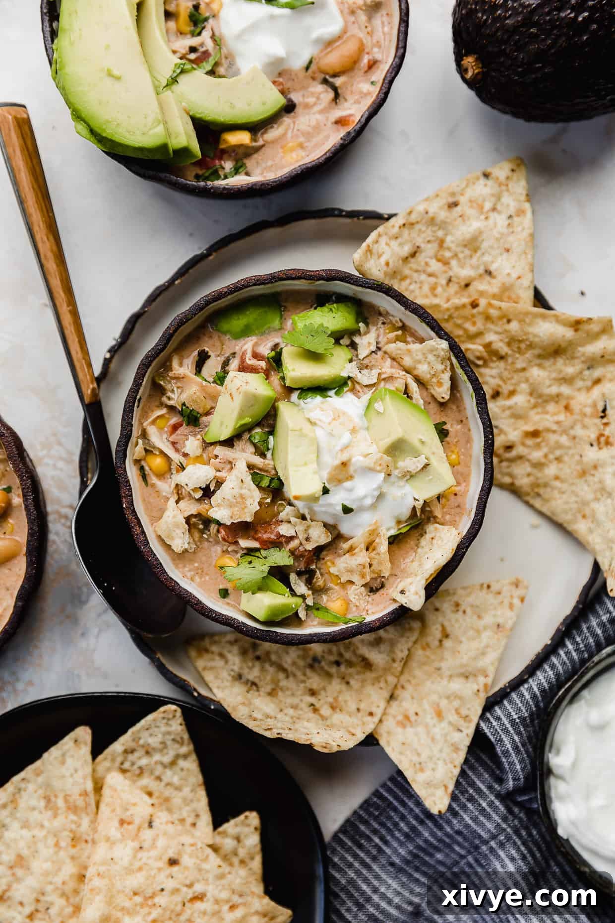 Crock Pot Cream Cheese Chicken Chili in a black bowl with tortilla chips, avocado, and sour cream on top, ready to be served.