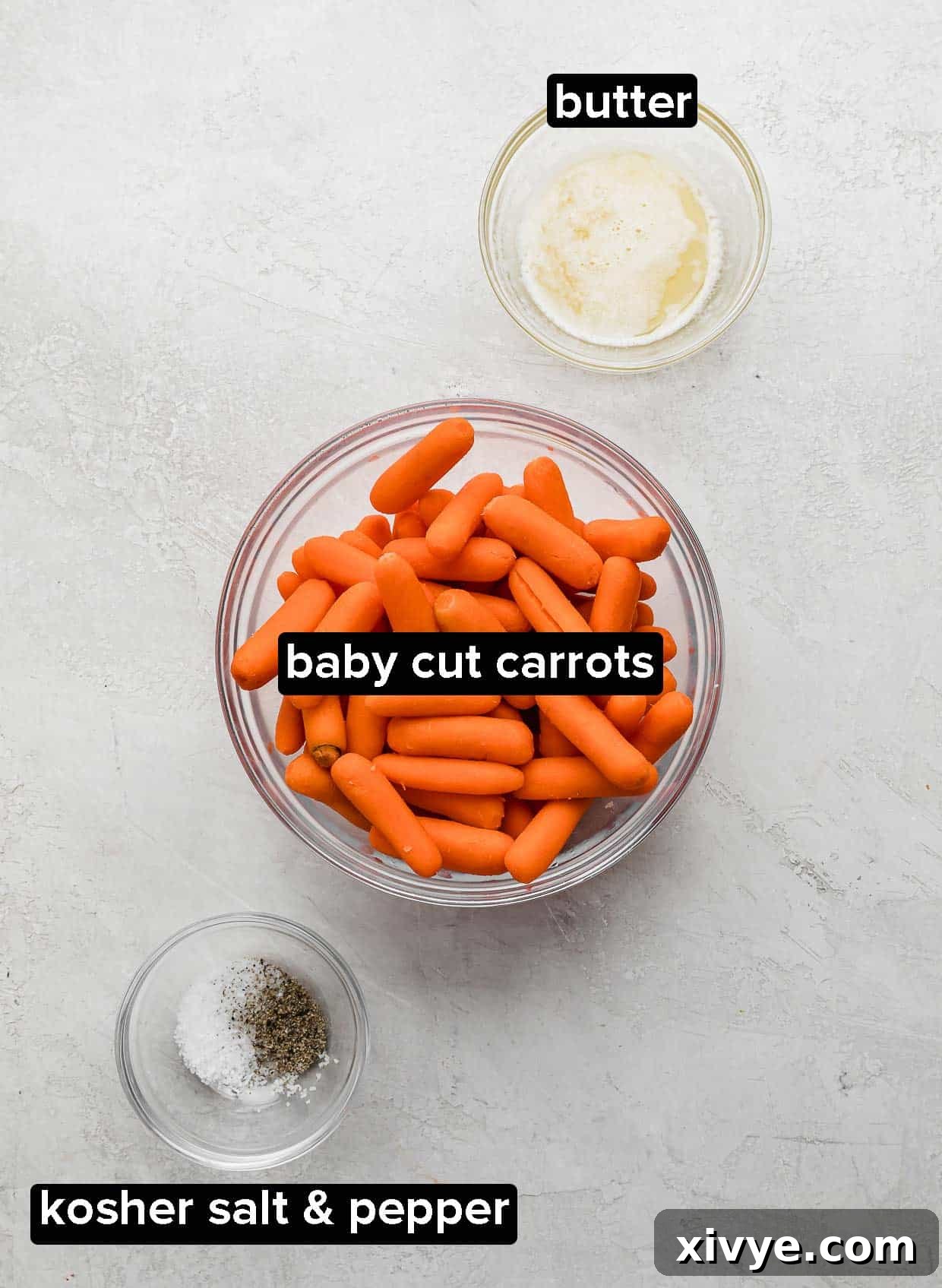 A white background with baby carrots in a glass bowl, butter, and salt and pepper.