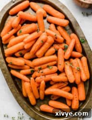 Roasted Baby Carrots topped with thyme and parsley on a bronze oval plate.