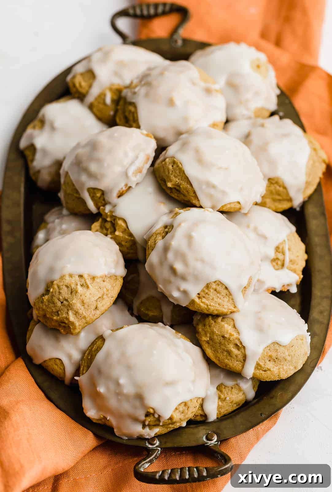 A tray on an orange napkin, stacked with glazed pumpkin cookies.