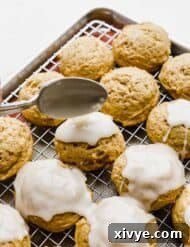 A spoon drizzling glaze over a pumpkin cookie.
