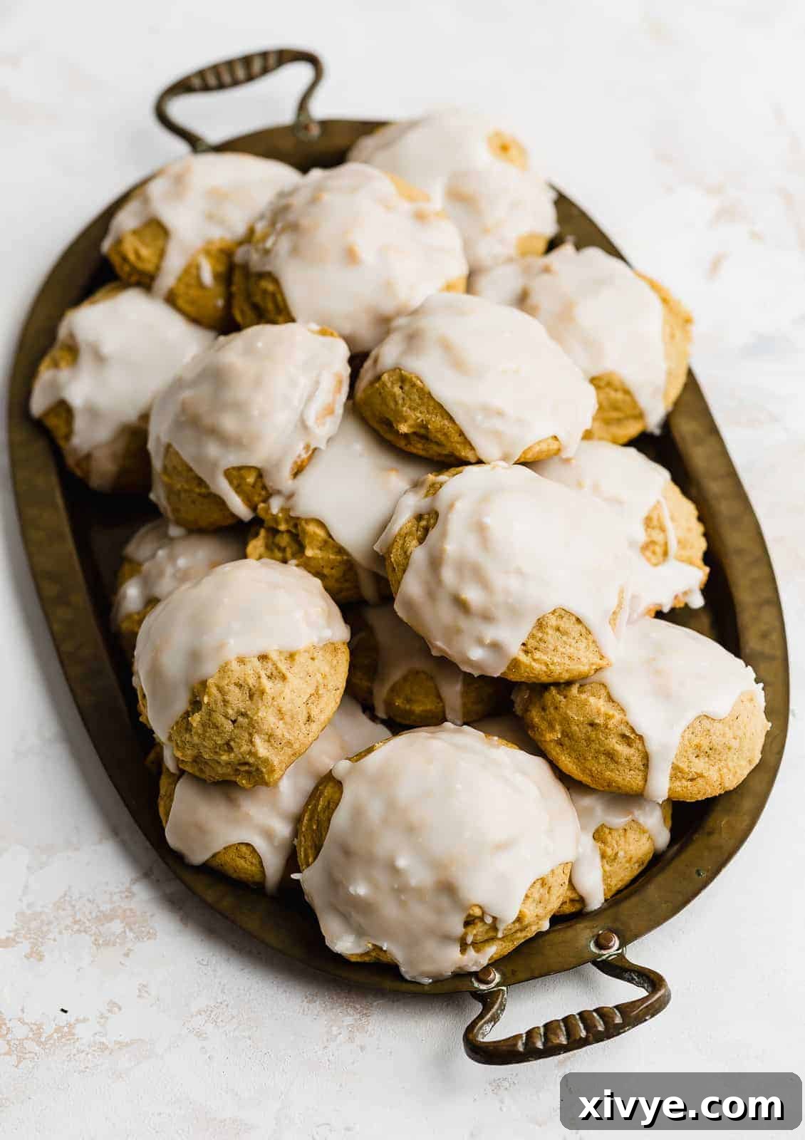 Glazed pumpkin cookies on a brass tray, against a white background.