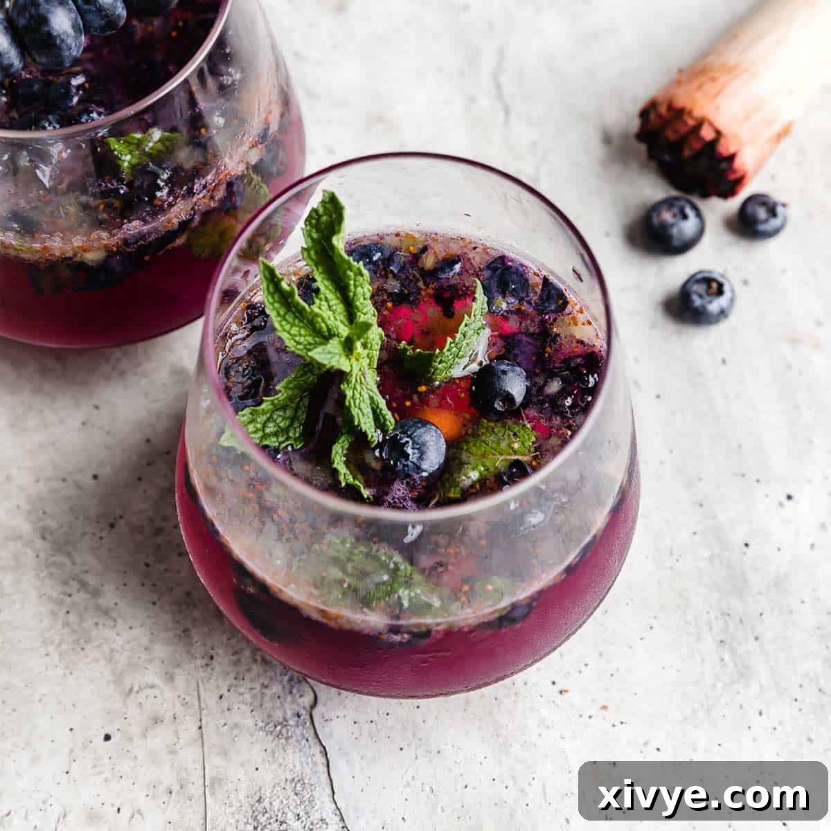 A glass cup on a gray background filled with a blueberry mojito mocktail.