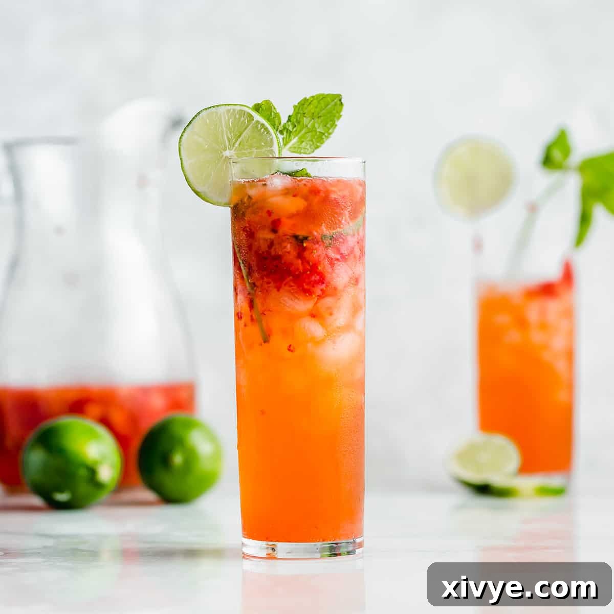 A tall mojito glass filled with a strawberry mojito mocktail with a lime wedge on the rim.