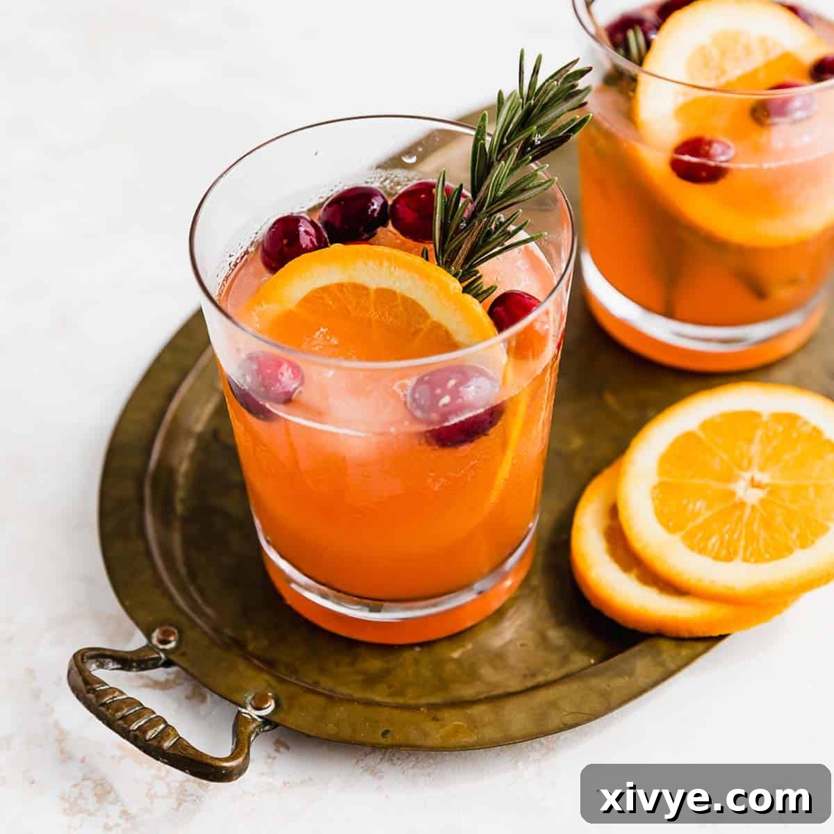 A clear glass filled with Christmas Slush Punch fresh cranberries and an orange slice.
