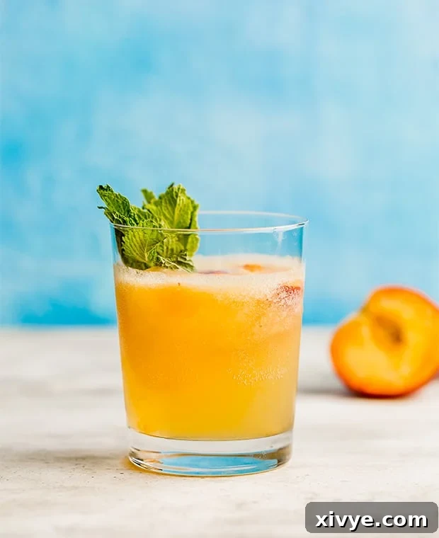 A glass full of peach punch in front of a blue background.