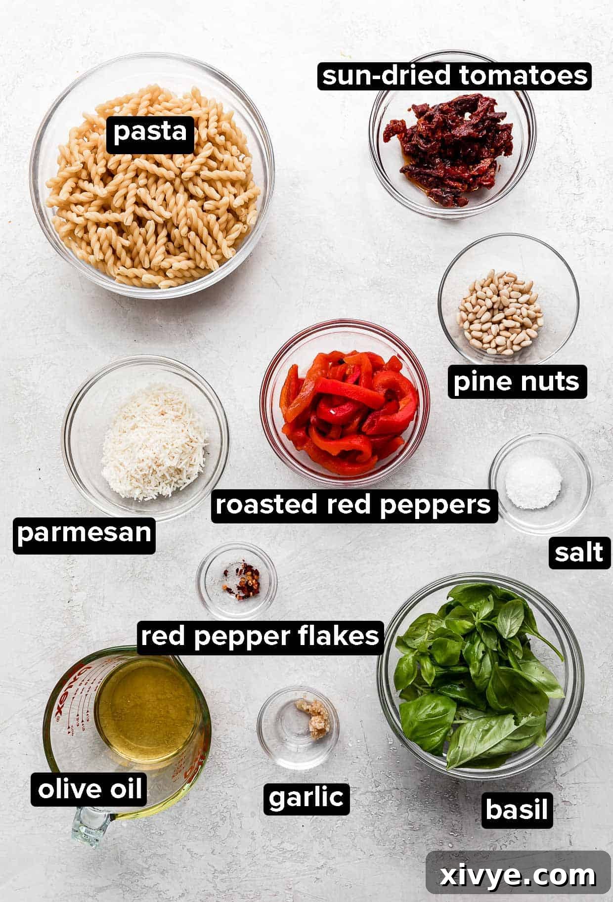 Red Pesto Pasta ingredients portioned into glass bowls on a light gray background. 