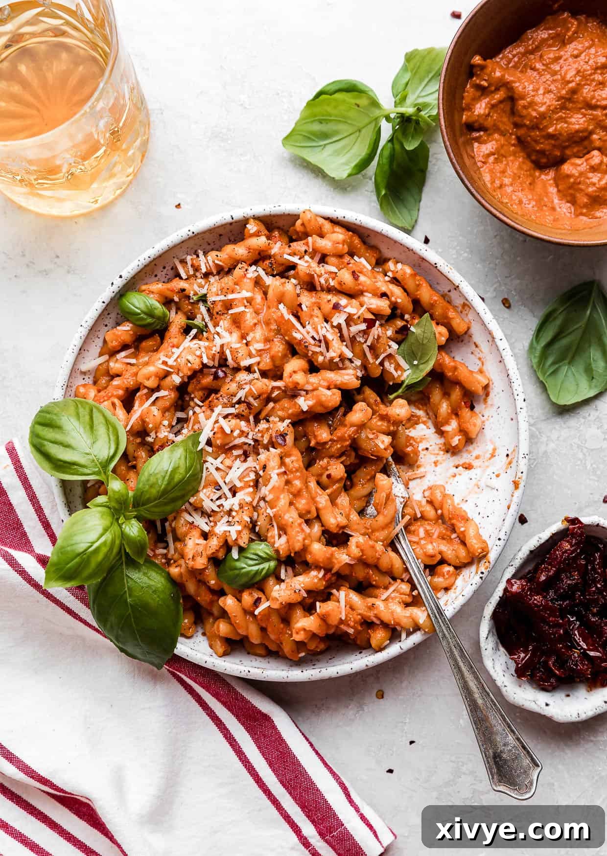 A fork in a bowl of Red Pesto Pasta topped with fresh basil.