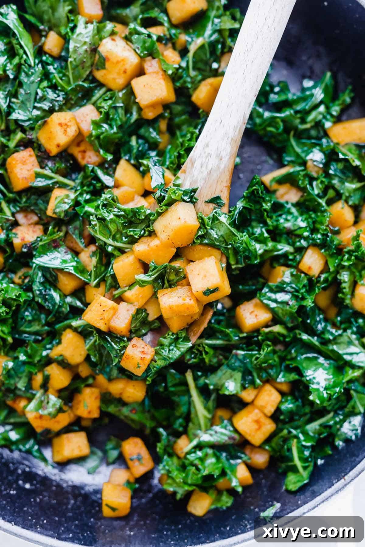 Butternut Squash and Kale Delight 6 Butternut Squash and Kale in a skillet with a wooden spoon scooping up some of the dish, highlighting the completed meal.