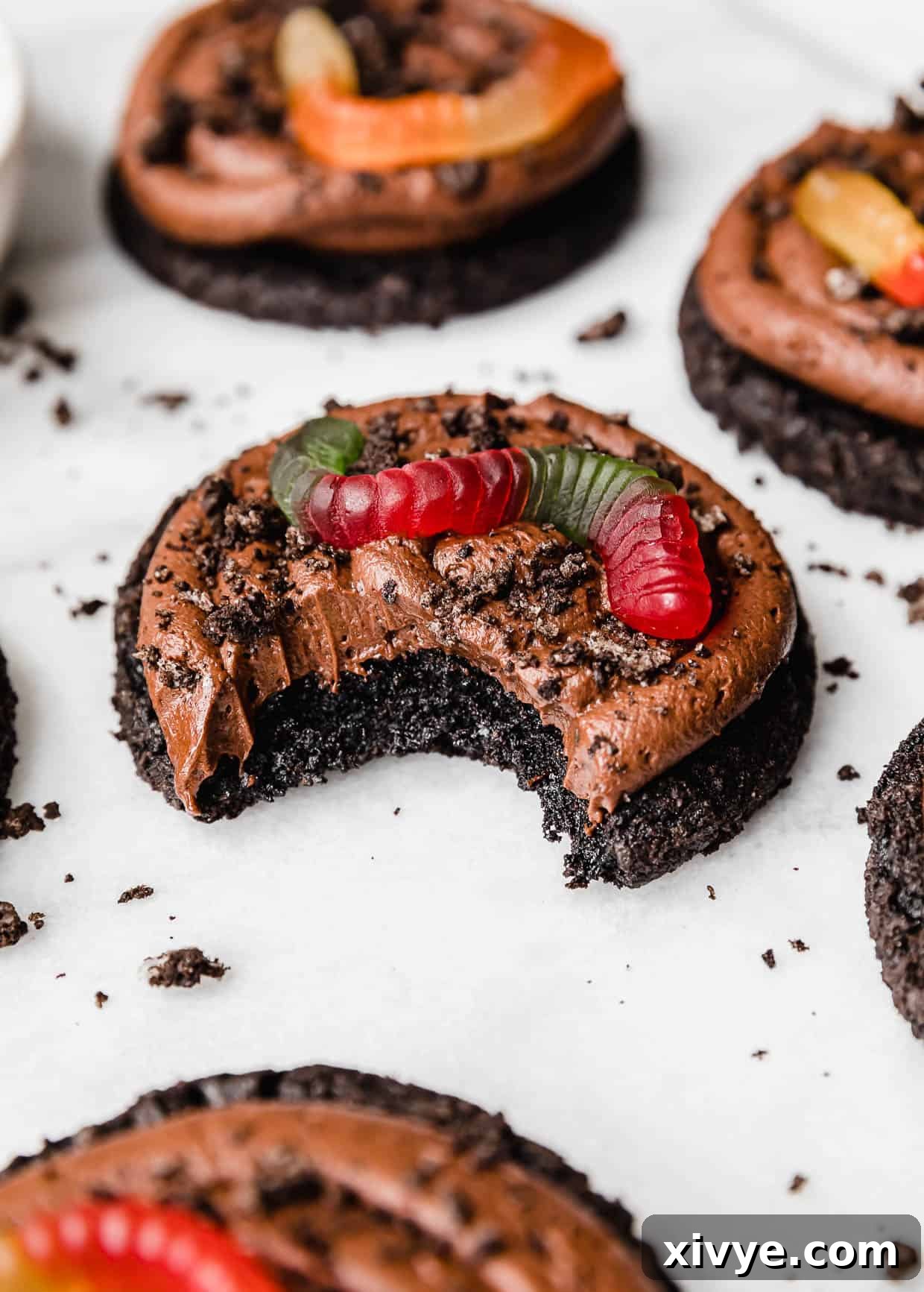 A Dirt Cake Cookie topped with Oreo crumbs and gummy worm with a bite taken out of the cookie.