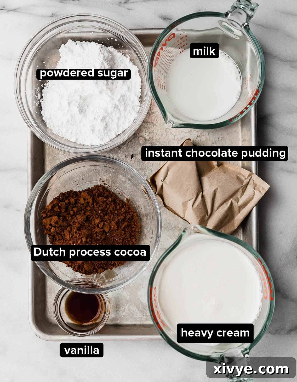 Dirt Cake Cookie frosting ingredients on a white background: cocoa powder, milk and heavy cream, instant chocolate pudding, powdered sugar, and vanilla.