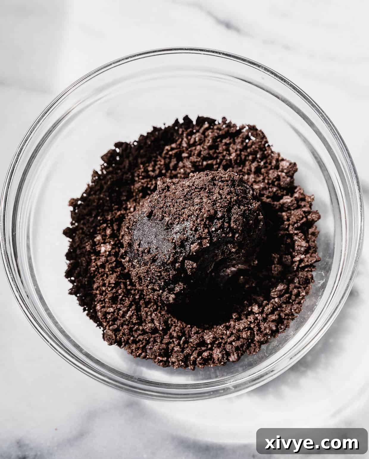 A black Oreo based cookie dough rolled in a ball in a bowl filled with crushed Oreo crumbs.