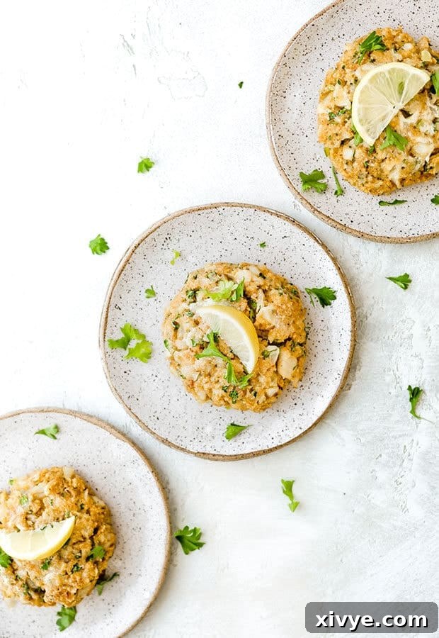 Crispy Tilapia Patties 2 Three golden-brown tilapia cakes served on separate plates, each garnished with a fresh lemon wedge and a sprig of parsley.