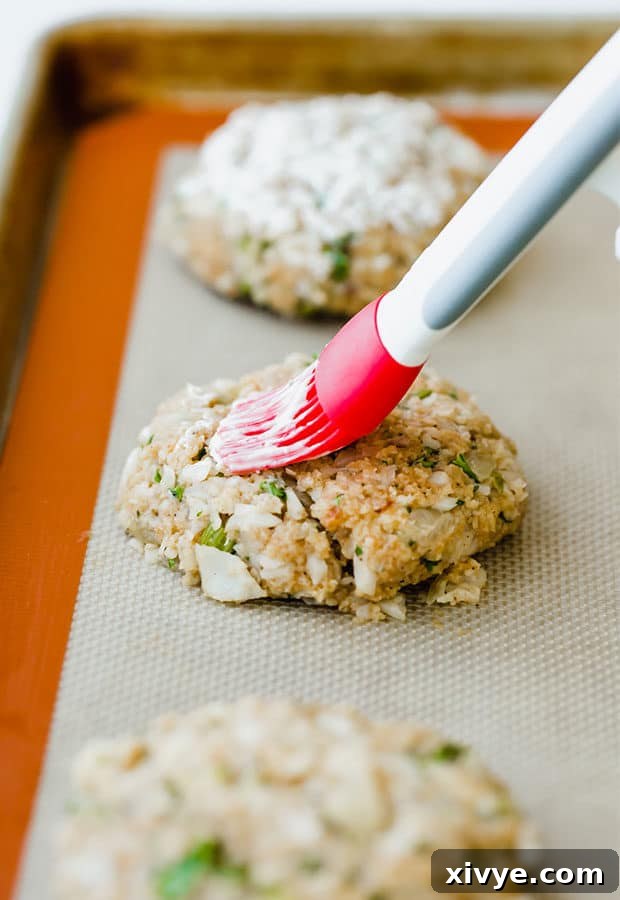 Crispy Tilapia Patties 6 A baking sheet of tilapia cakes with a pastry brush gently spreading a thin layer of mayonnaise over each patty before baking.